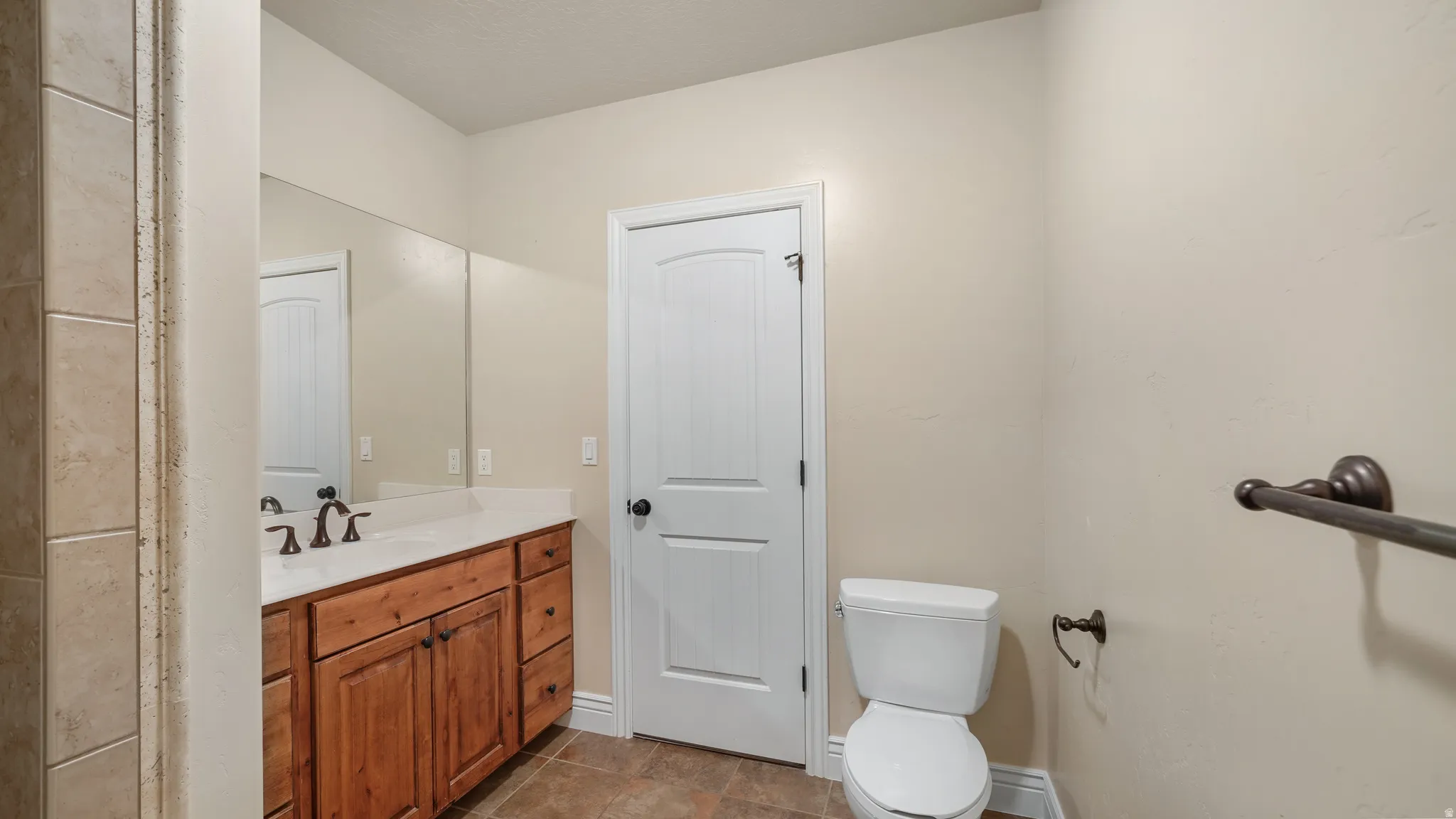 Bathroom featuring a wood vanity with a light-colored countertop and integrated sink, a large wall-mounted mirror, ceramic tile flooring, and a shower with tiled walls