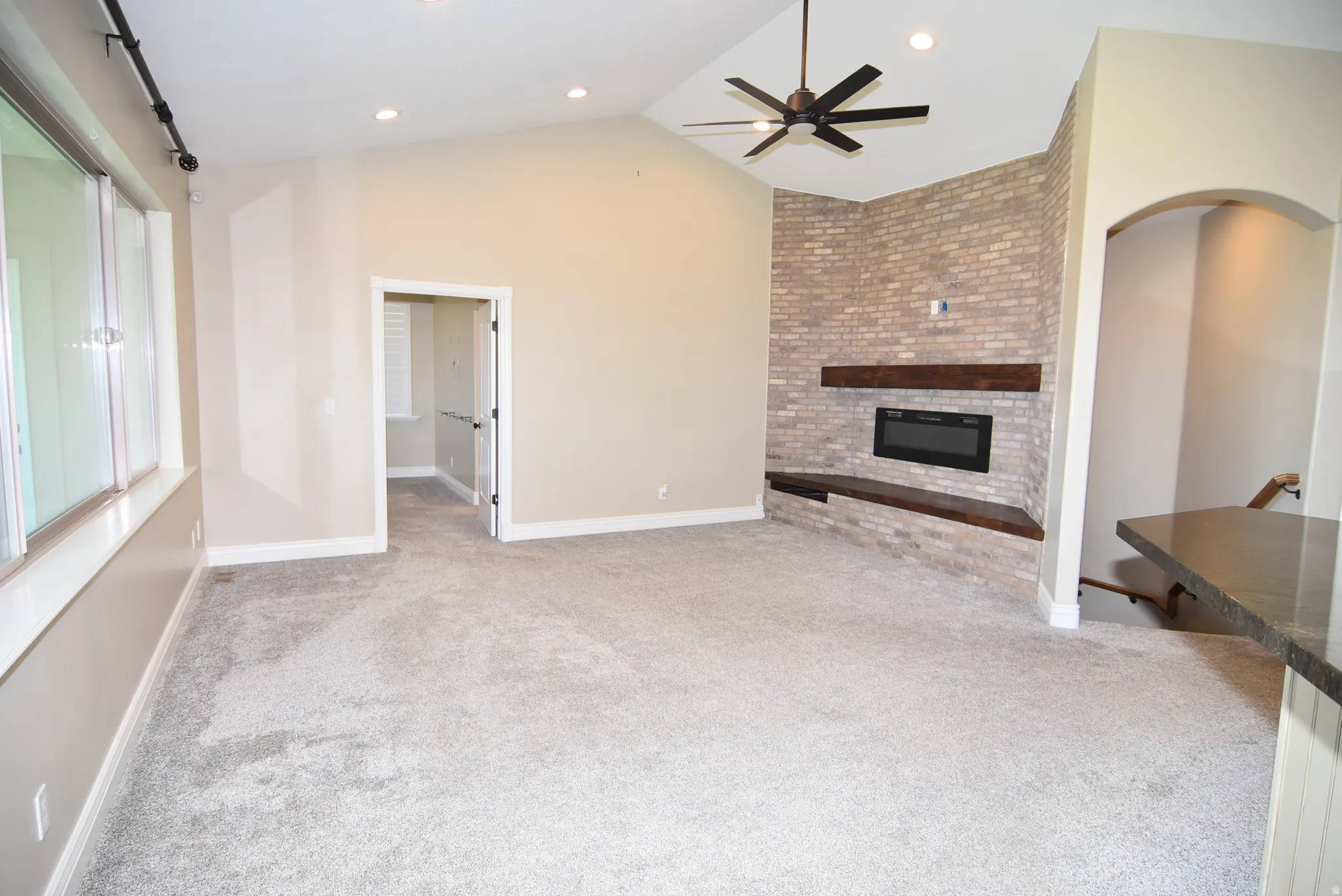 Living area featuring vaulted ceilings, a contemporary electric fireplace with a brick surround, and a ceiling fan