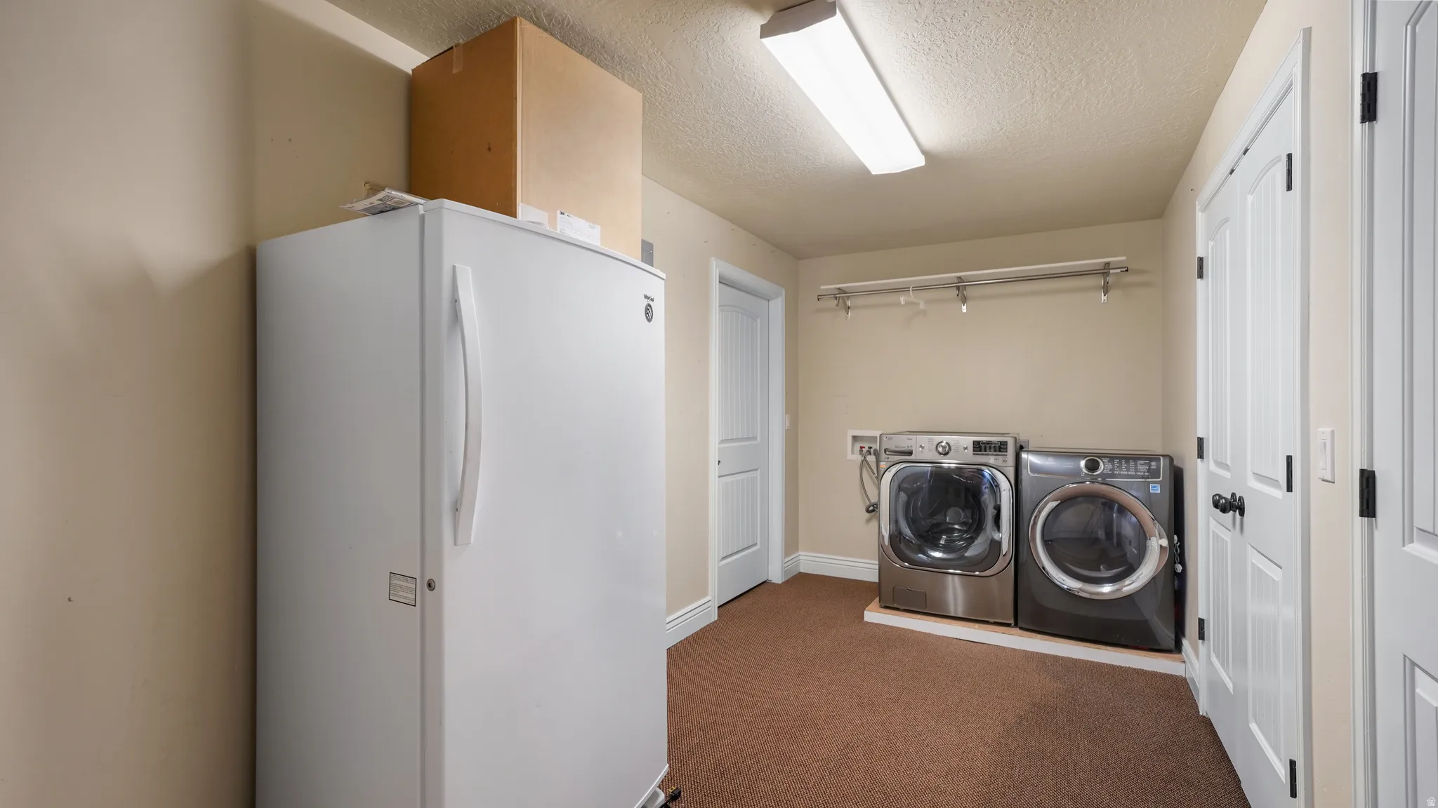 Dedicated utility room featuring front-loading laundry machines and overhead garment rack