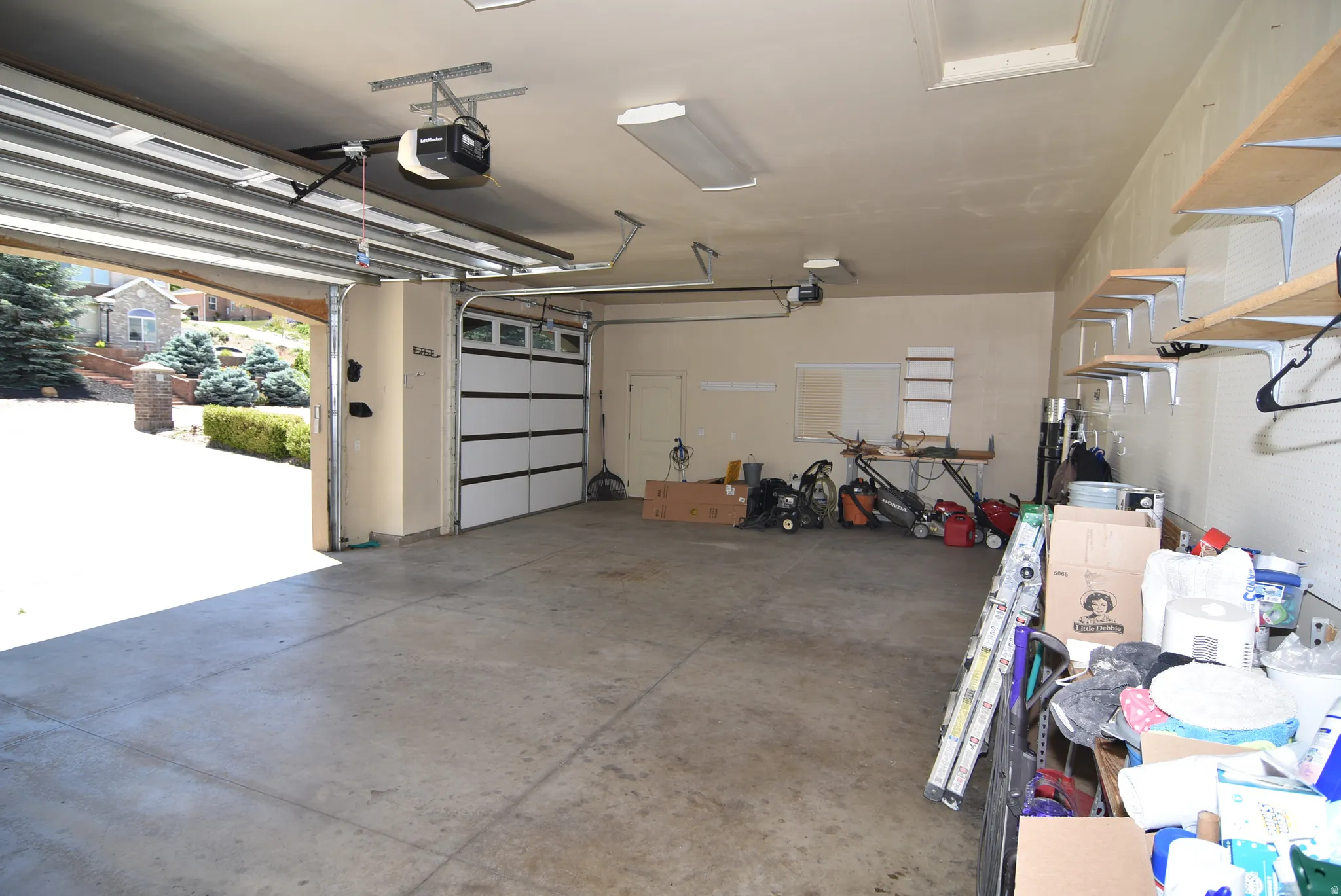 Spacious two-car garage featuring a concrete floor, automatic garage door openers, and built-in wall shelving for storage