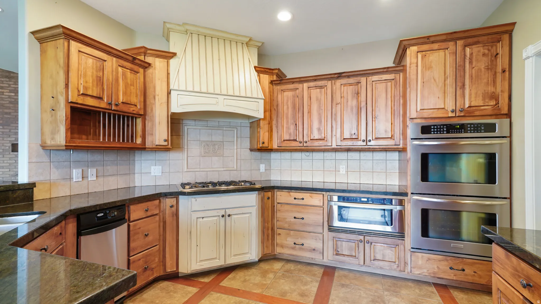 Kitchen featuring custom wood cabinetry, granite countertops, tile flooring, stainless steel double ovens, and a built-in gas cooktop with a custom range hood
