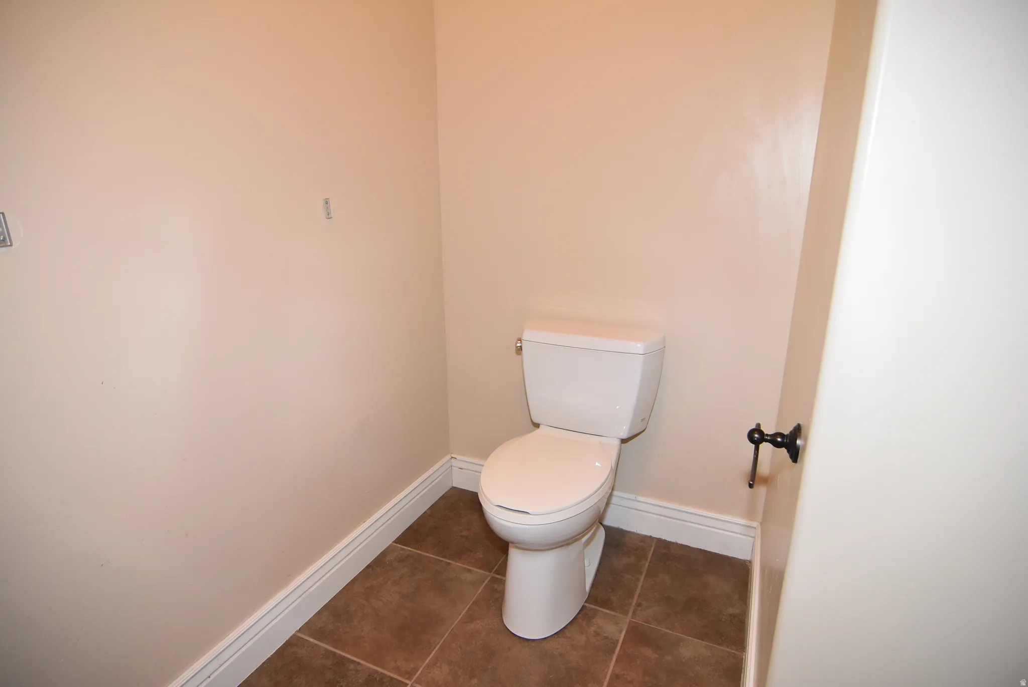 Powder room featuring a standard white toilet, brown tile flooring, and light-toned walls with white baseboards