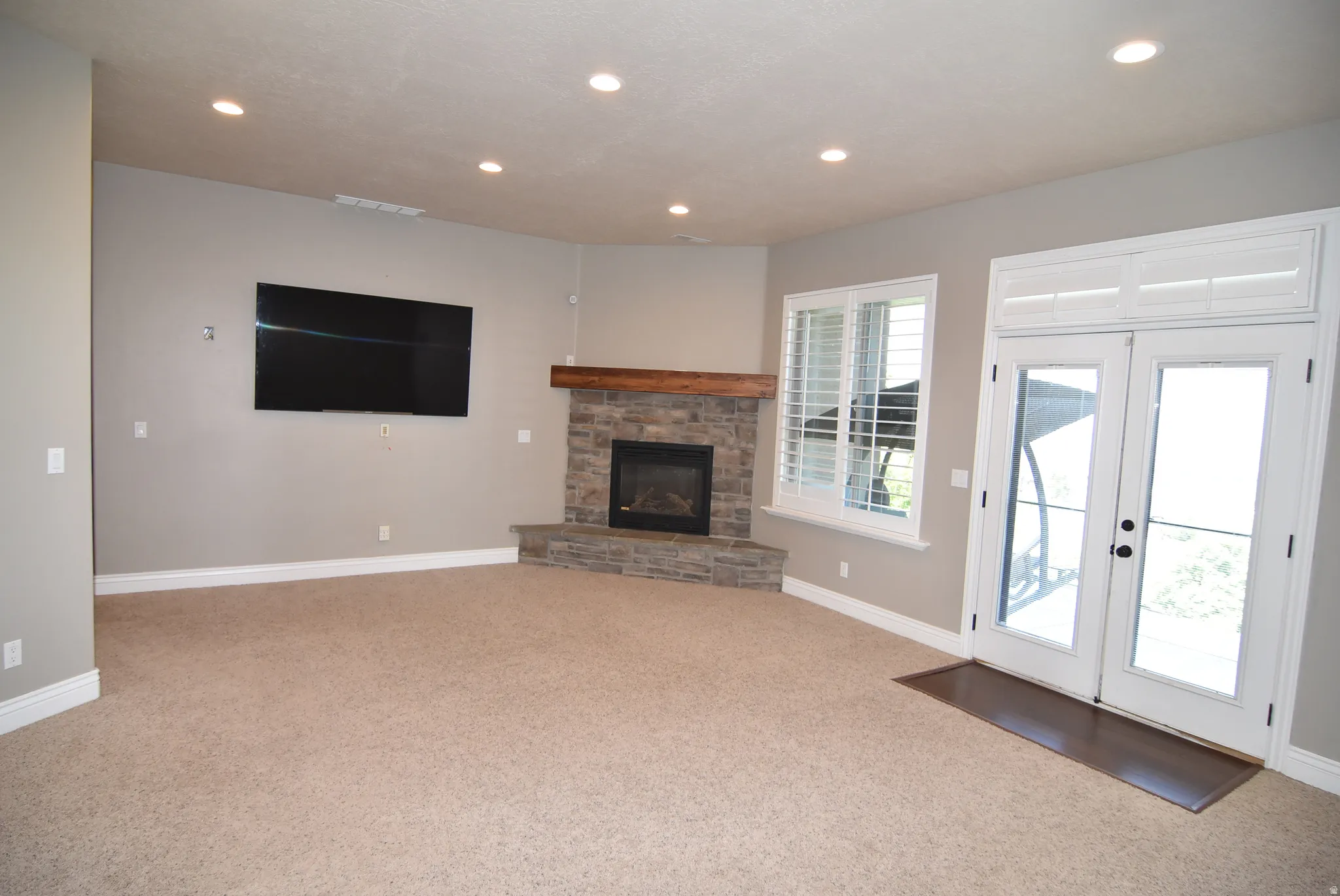Spacious room featuring a stone-faced corner fireplace with a wood mantel, Daylight windows, French doors to walk-out basement and back patio, recessed lighting, and a neutral carpet
