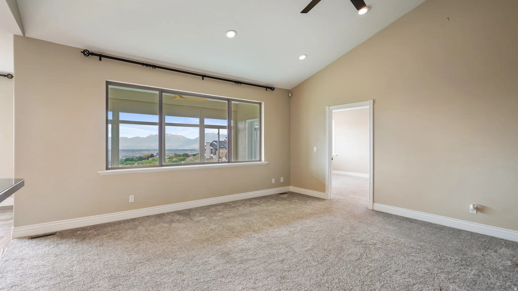 Spacious living area featuring a large picture window, vaulted ceiling, recessed lighting, ceiling fan, and light gray carpet