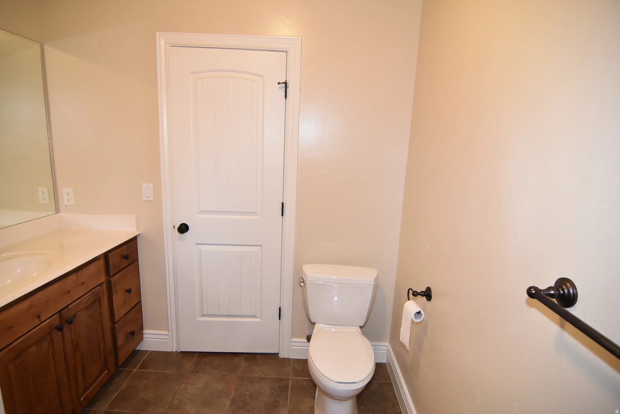 Bathroom featuring a wood-finish vanity with a single basin, a white toilet, and dark tile flooring