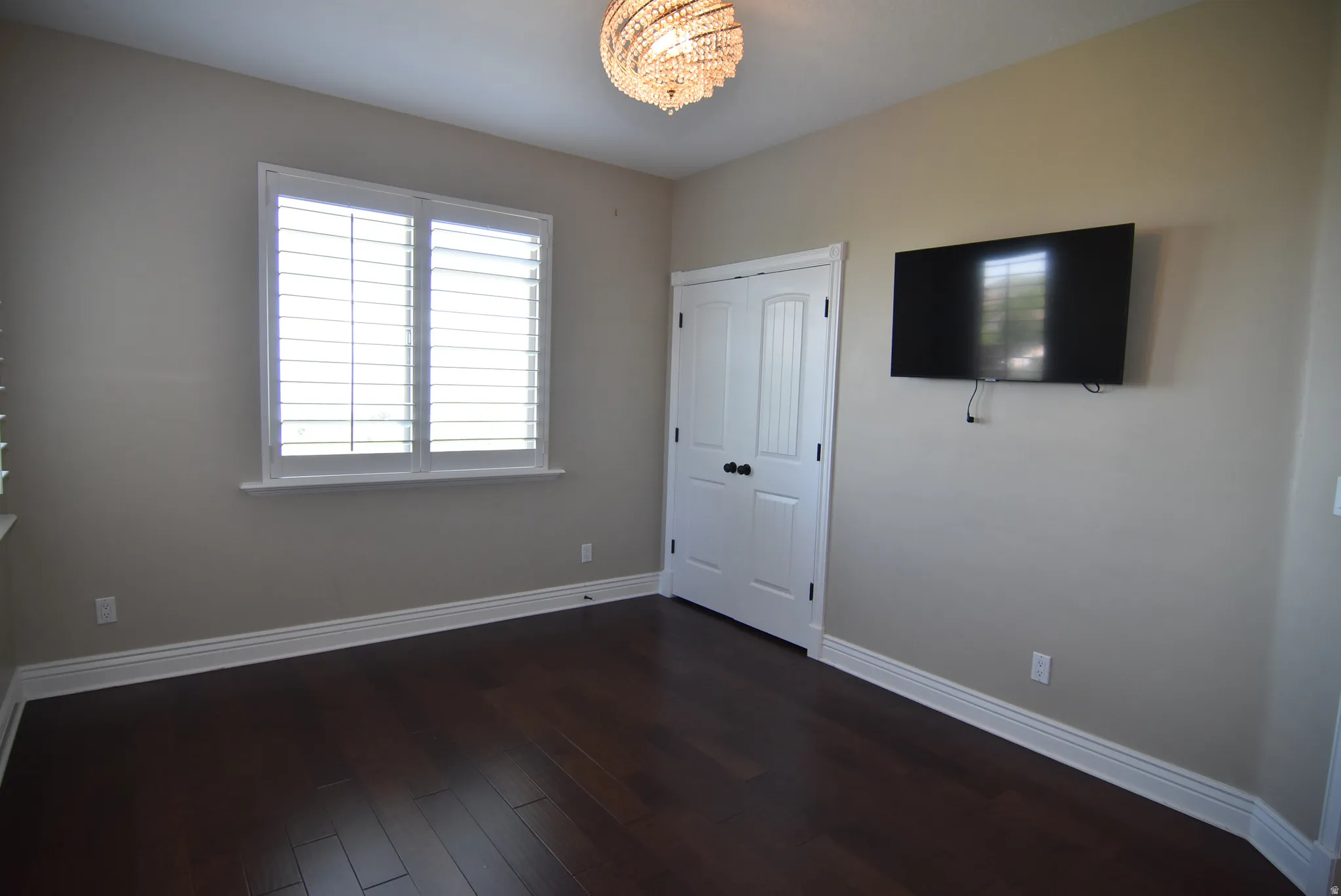 Bedroom #2 witHardwood flooring complements neutral wall tones in this room featuring a window with white plantation shutters, a double-panel door, and a decorative ceiling light fixture