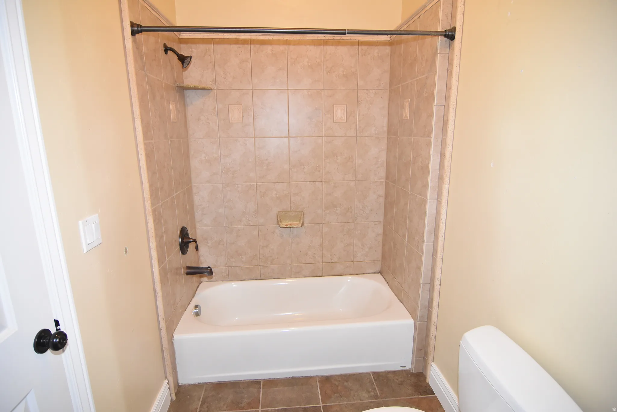 Bathroom with a white bathtub, bronze-finish fixtures, and light-toned tile surround