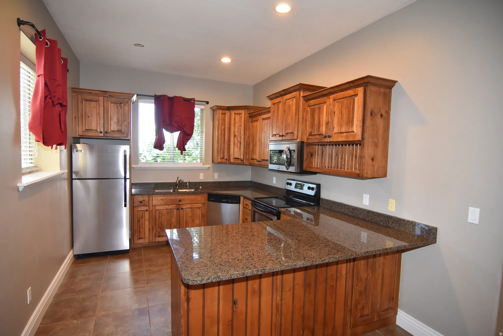 Kitchen featuring wood-finish cabinetry, granite countertops, stainless steel refrigerator, built-in microwave, and tile flooring