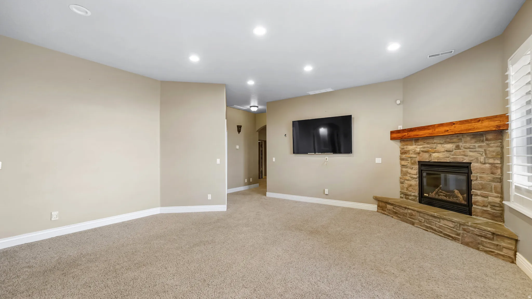 Spacious living area featuring a corner stone fireplace with a substantial wood mantel