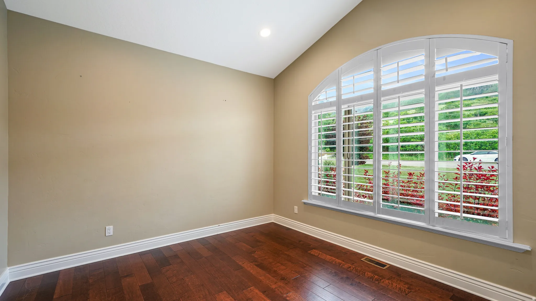 Arch-top window with plantation shutters, featuring wood-finish flooring, vaulted ceiling, recessed lighting, and white baseboards