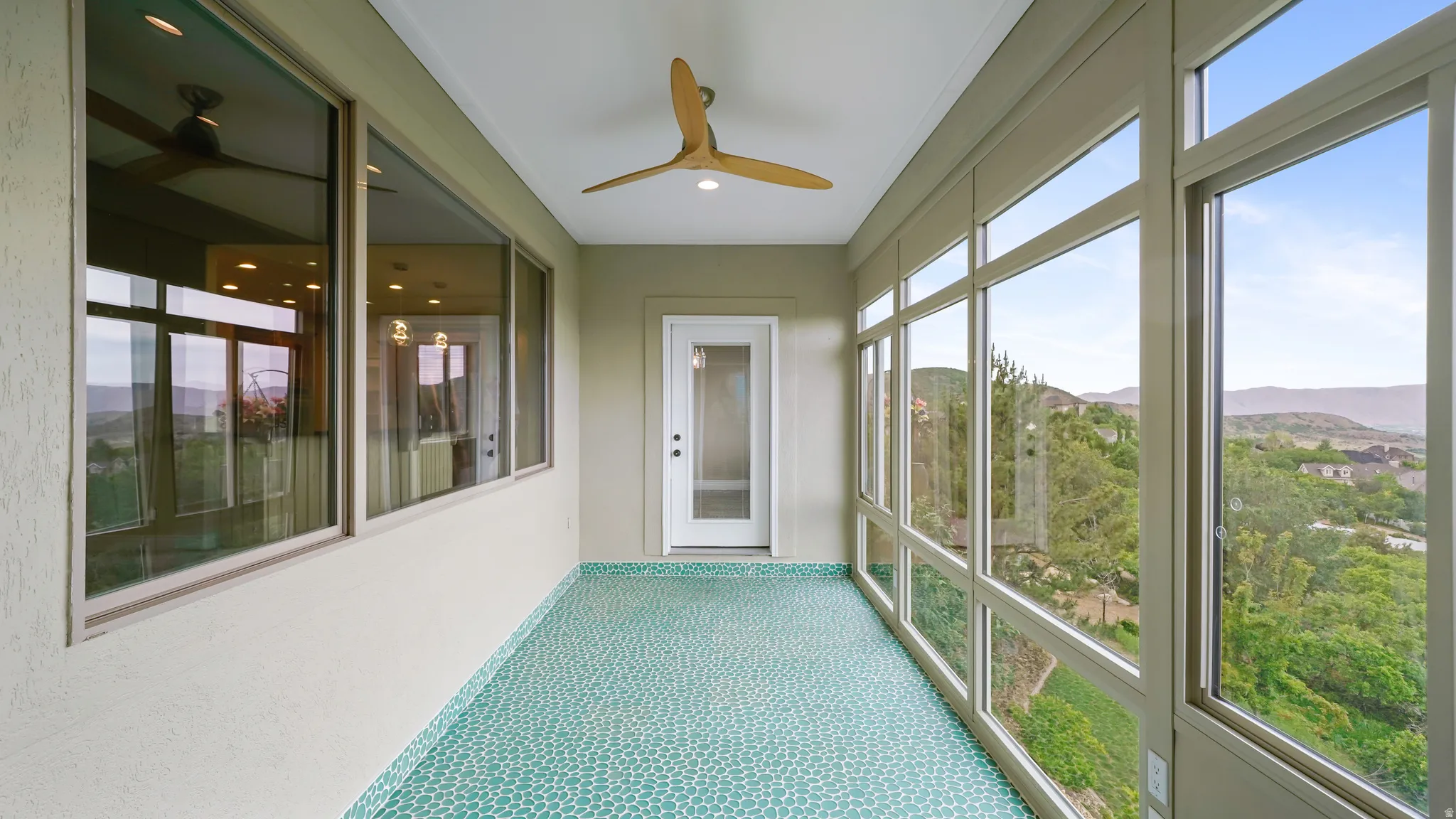 Expansive sunroom featuring floor-to-ceiling windows, a mosaic tile floor, and a modern ceiling fan