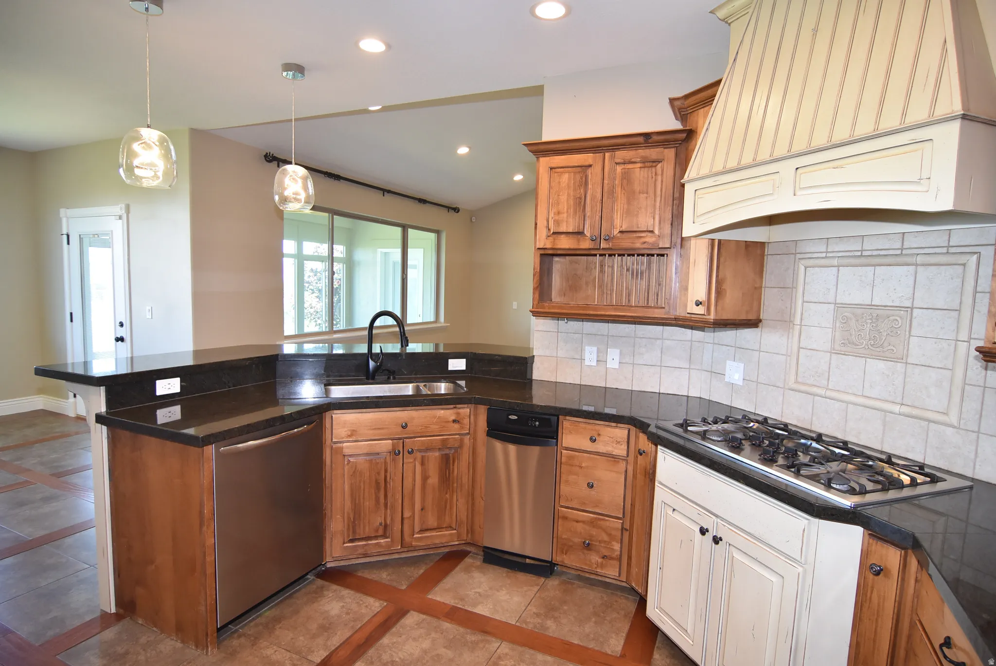 Kitchen featuring dark countertops, stainless steel appliances, wood-finish cabinetry, and a decorative range hood