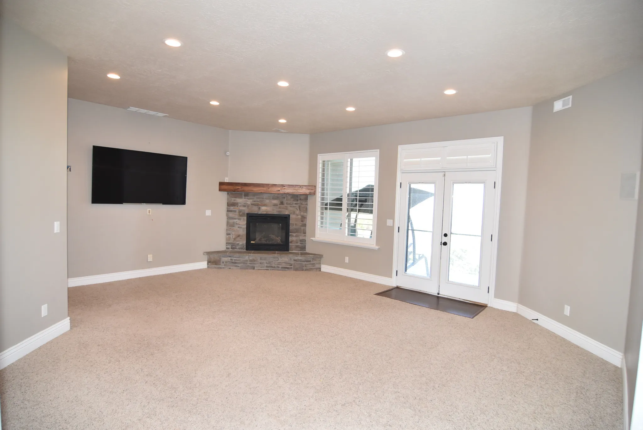 Spacious living area featuring a corner stone fireplace with a wood-beam mantle, recessed lighting, carpet flooring, and white double doors