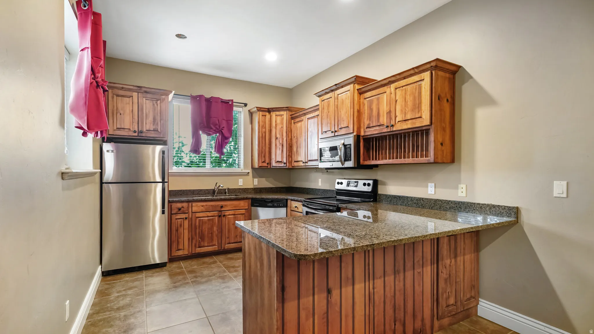 Kitchen featuring wood cabinetry, stainless steel appliances, speckled stone countertops, and tile flooring
