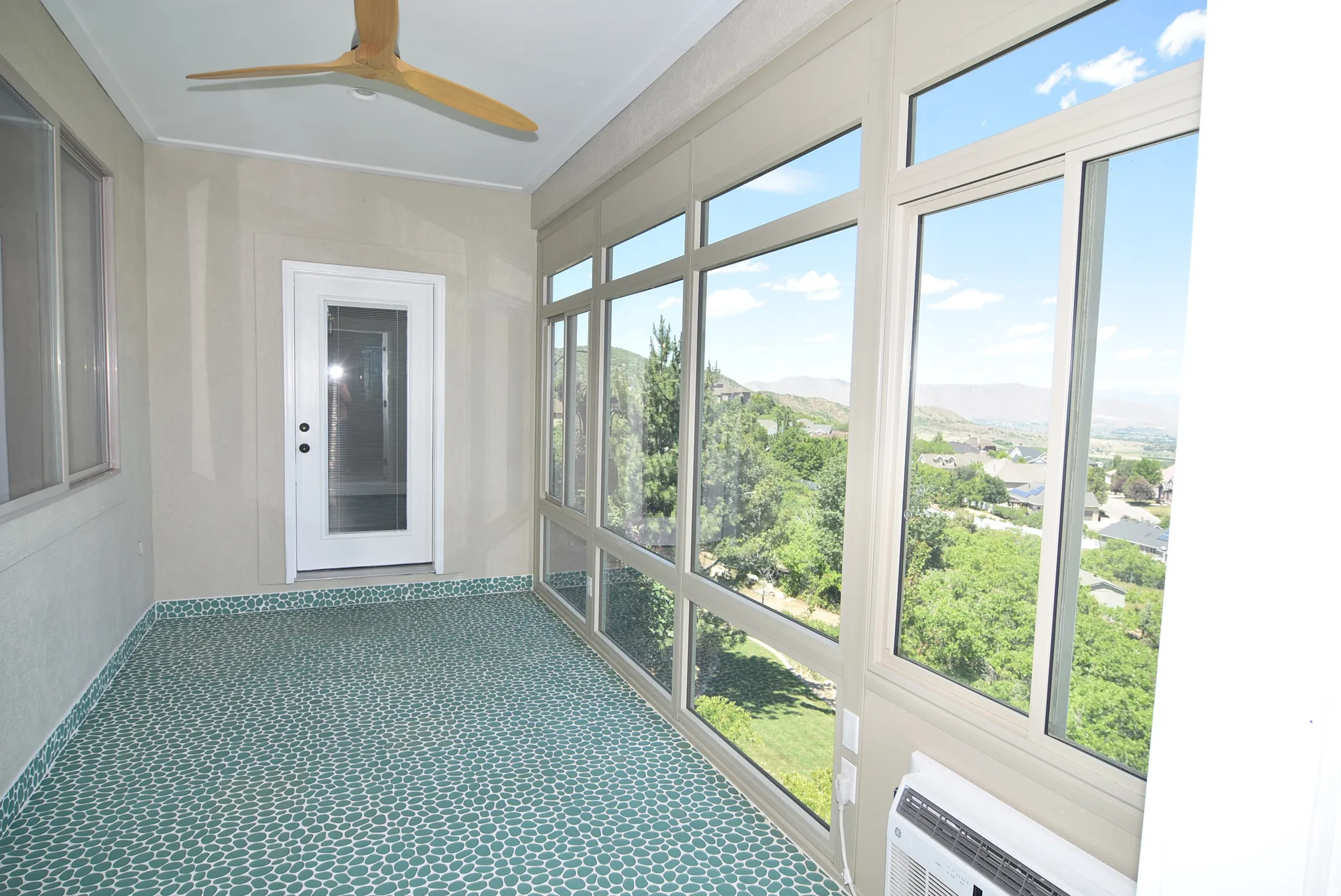 Enclosed sunroom featuring expansive windows overlooking a verdant landscape and distant hills