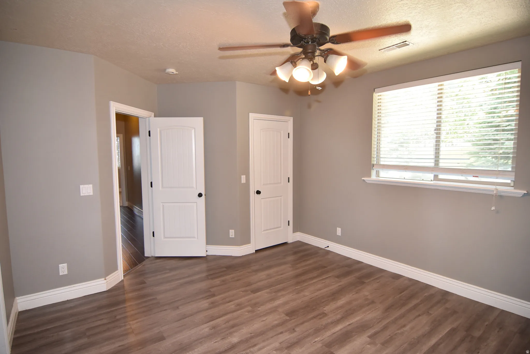 Spacious room featuring wood-finish flooring, neutral gray walls, and white baseboards