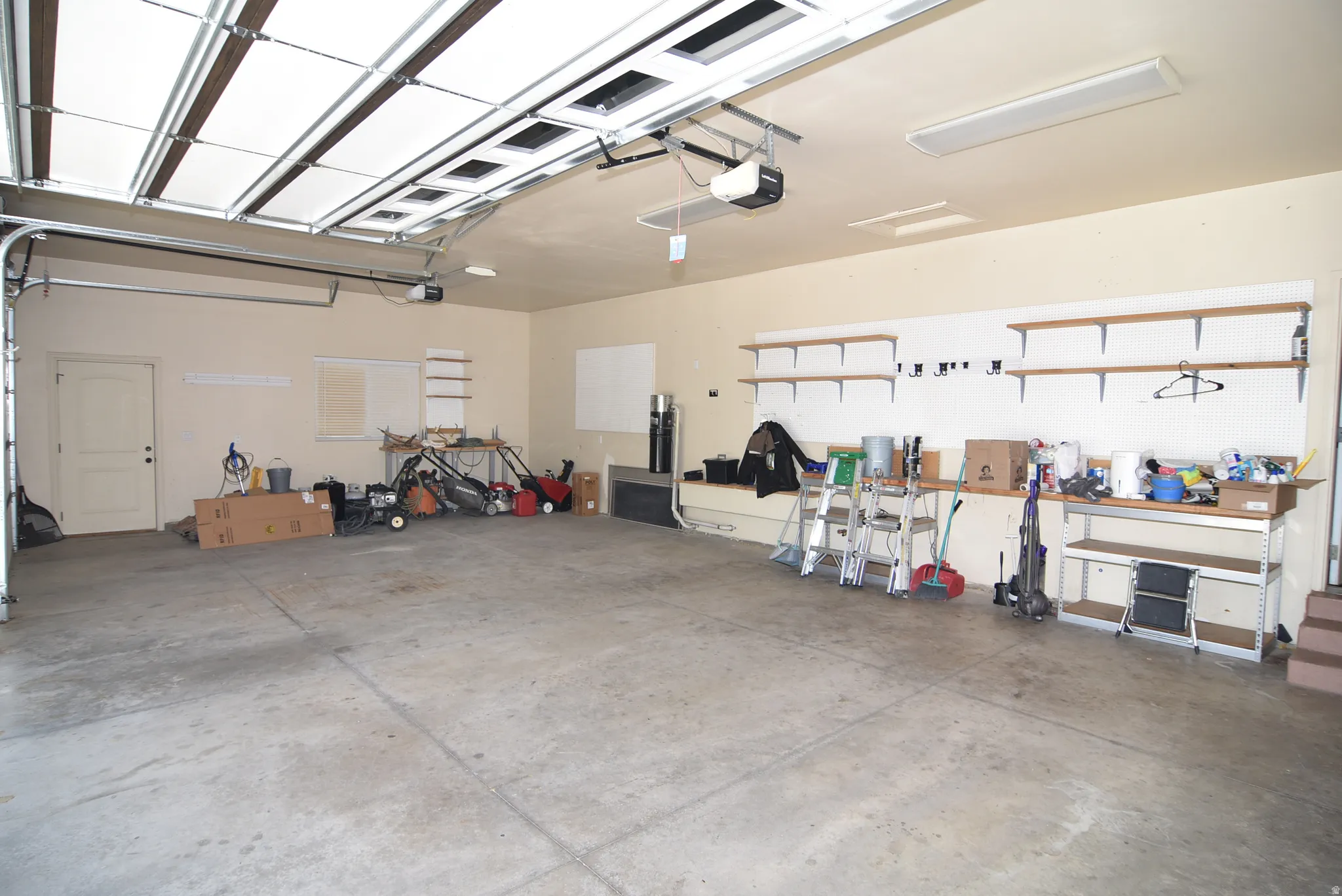Spacious garage featuring a concrete floor, built-in shelving, pegboard storage, and an automatic garage door opener