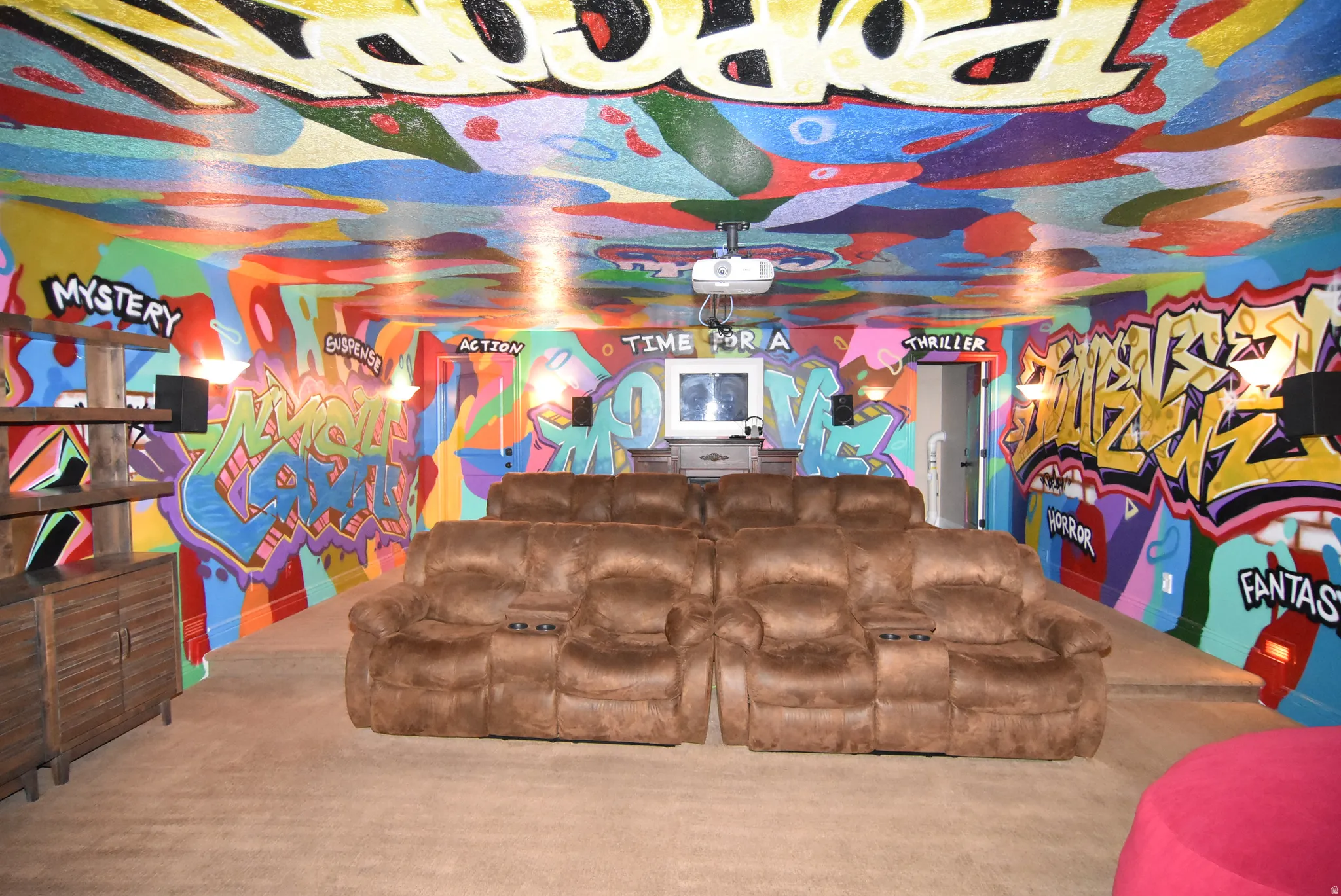 Vibrantly decorated entertainment space featuring a projector and screen, built-in shelving, sconce lighting, and wall-to-wall carpeting