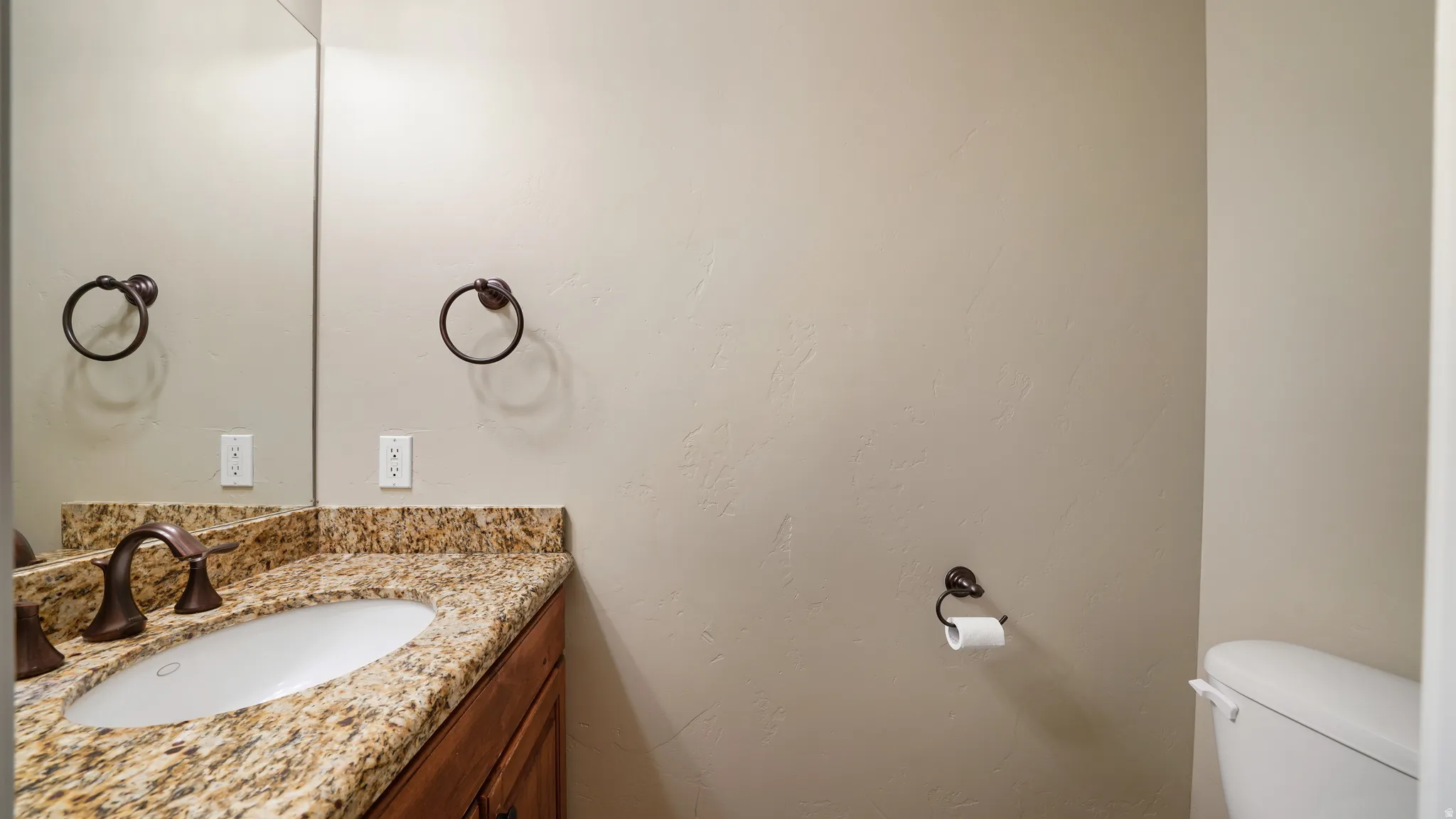 Vanity featuring a stone countertop, undermount sink, and bronze-finish faucet