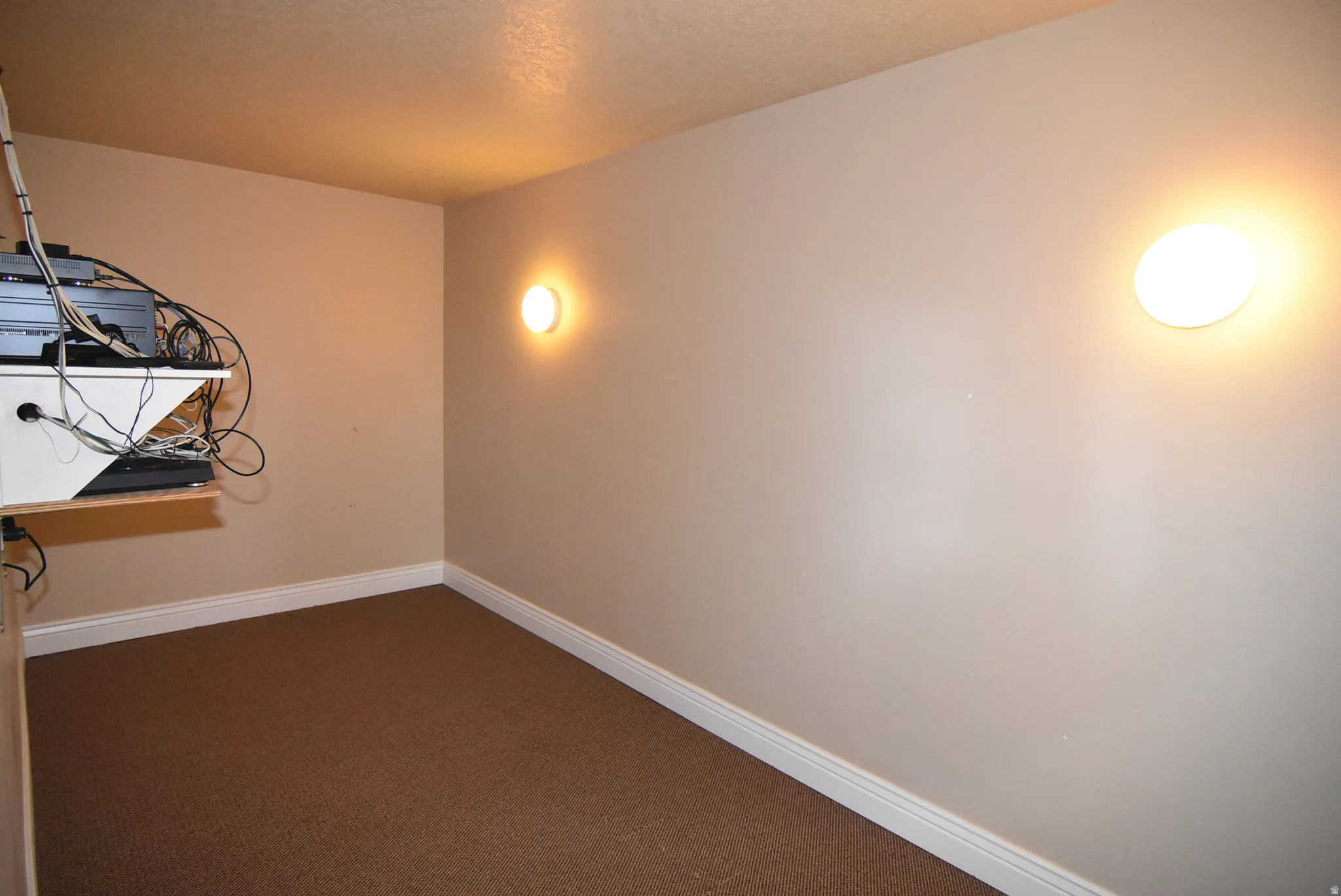 AV equipment inCarpeted room featuring neutral wall paint, white baseboards, and two wall-mounted circular light fixtures