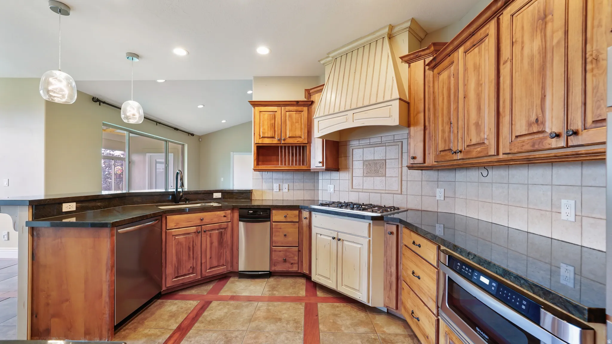 Kitchen featuring wood cabinetry, dark countertops, a tile backsplash, and stainless steel appliances, including a built-in microwave and dishwasher