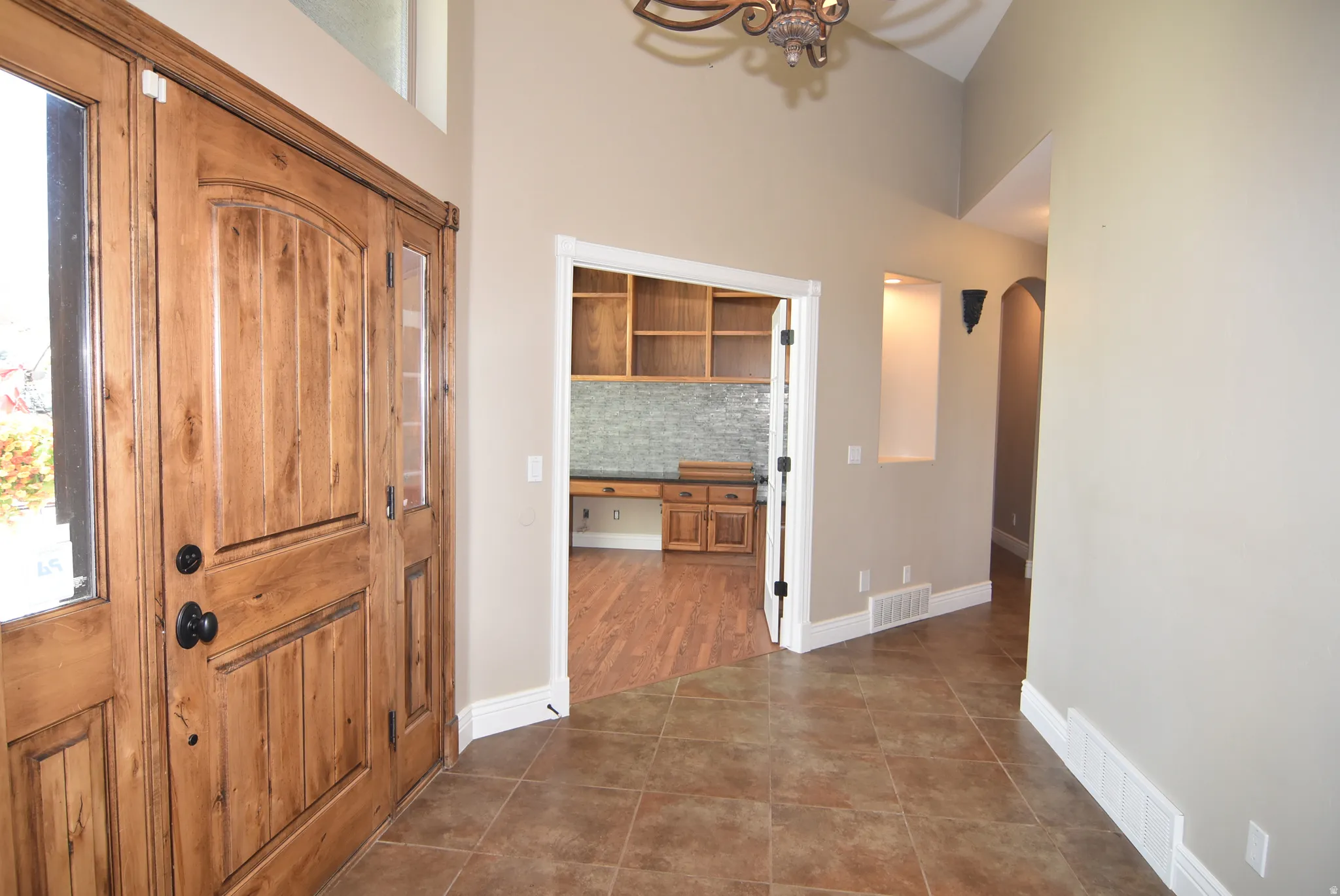 Foyer featuring solid wood entry doors with glass side panels, vaulted ceiling, and tile flooring