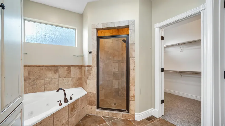 Bathroom featuring a jetted soaking tub with bronze fixtures, a walk-in shower with tile surround and glass enclosure, and an overhead transom window