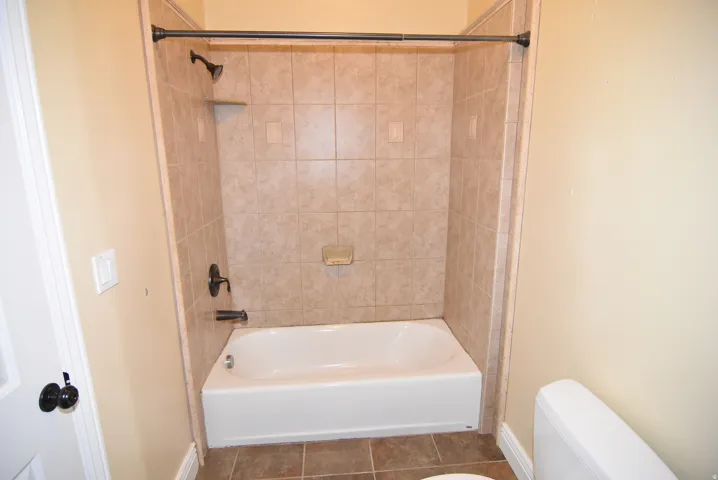 Bathroom with a white bathtub, bronze-finish fixtures, and light-toned tile surround