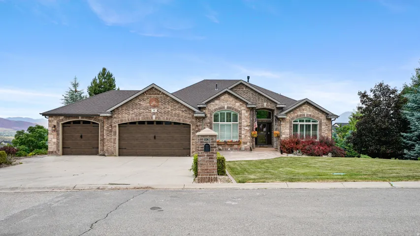 Brick exterior residence featuring a three-car garage, arched windows, and a landscaped front yard with established plantings