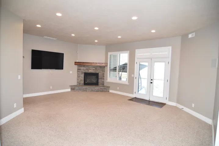 Spacious living area featuring a corner stone fireplace with a wood-beam mantle, recessed lighting, carpet flooring, and white double doors