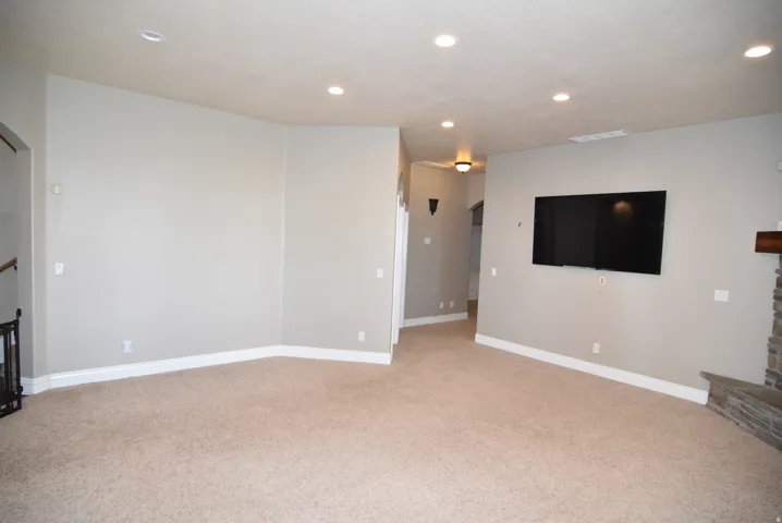 Spacious living area featuring neutral carpeting, light gray walls, white baseboards, and recessed ceiling lighting