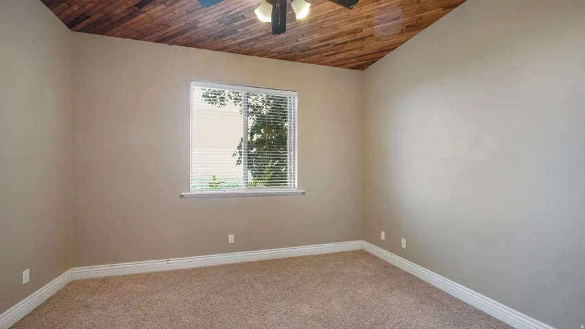 Room featuring wood-planked ceiling, textured carpeting, neutral wall color, and a window with horizontal blinds