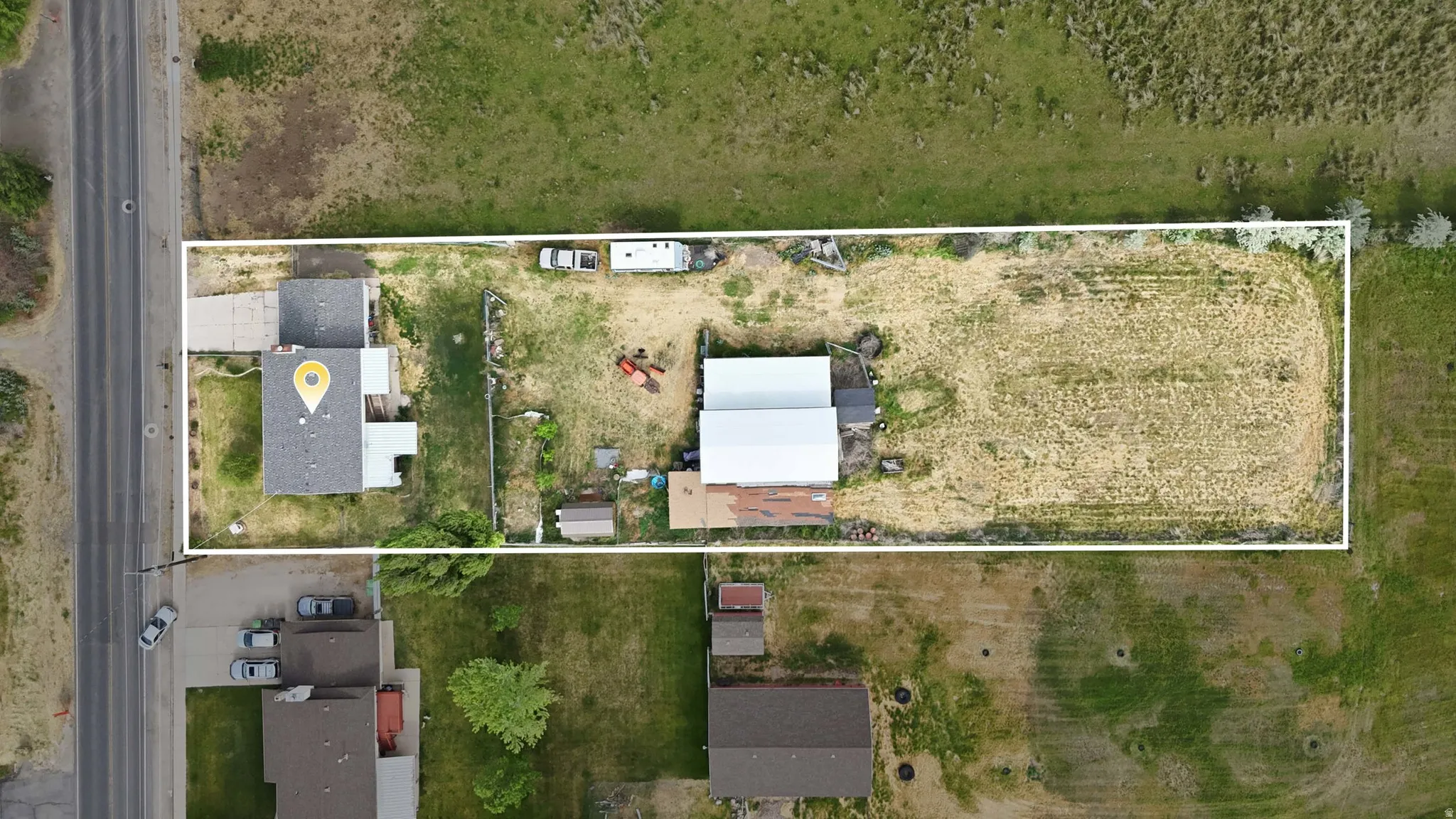 Expansive property featuring a residence with a gray shingle roof, a detached auxiliary building with a white metal roof, and a large undeveloped lot