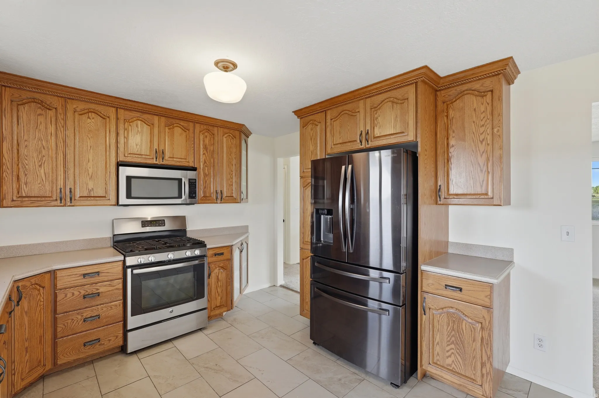 Kitchen featuring extensive wood cabinetry, stainless steel oven/range, built-in microwave, dark stainless steel refrigerator, and tiled flooring