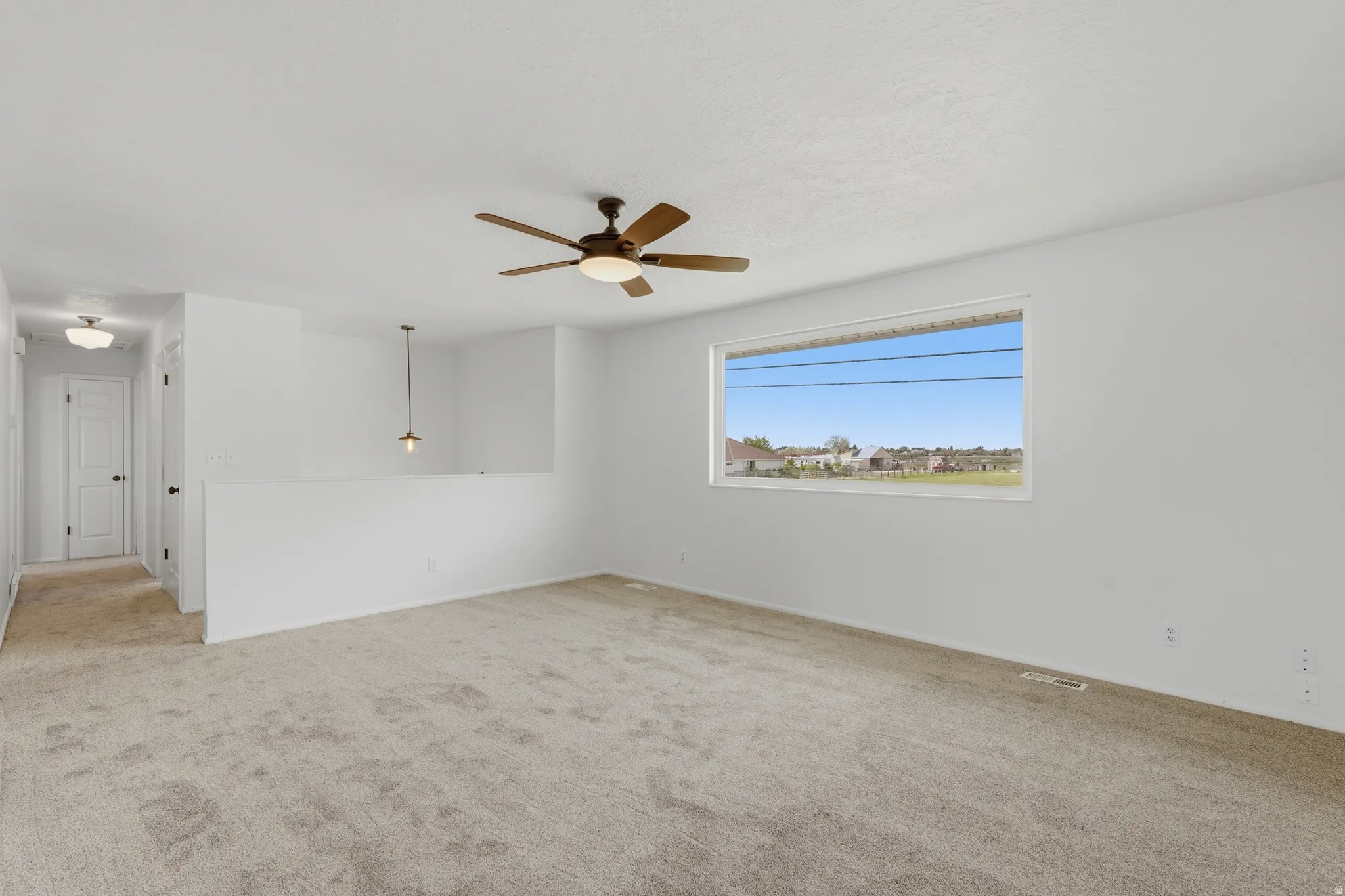 Spacious room featuring a large window, neutral carpeting, and a ceiling fan with integrated lighting