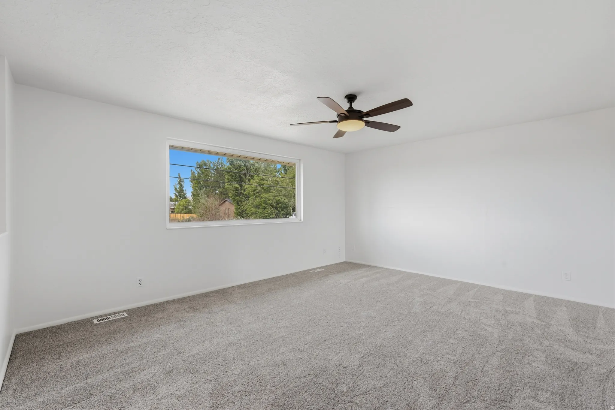 Spacious room with light gray carpeting, neutral white walls, and a large window