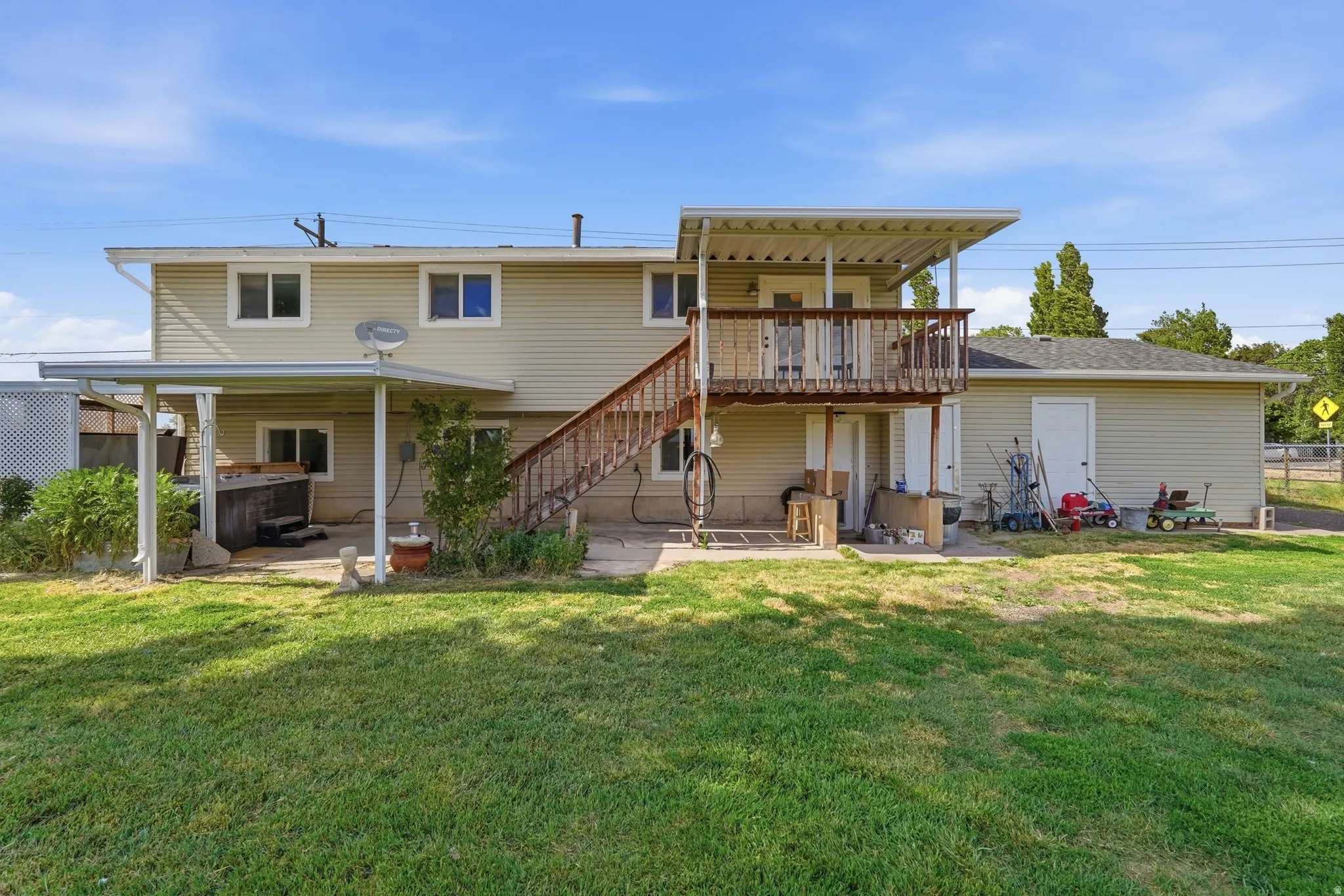 Expansive backyard featuring a large grassy area, a covered patio, and a second-story deck with wooden stairs