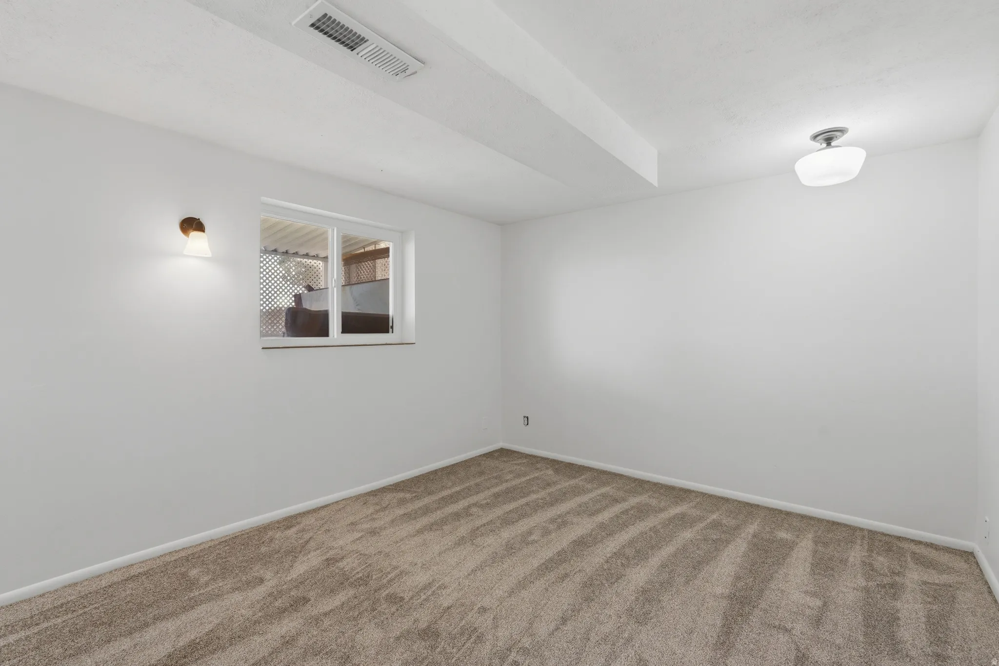 Carpeted room with a white window, a wall-mounted sconce, and a flush-mount ceiling light