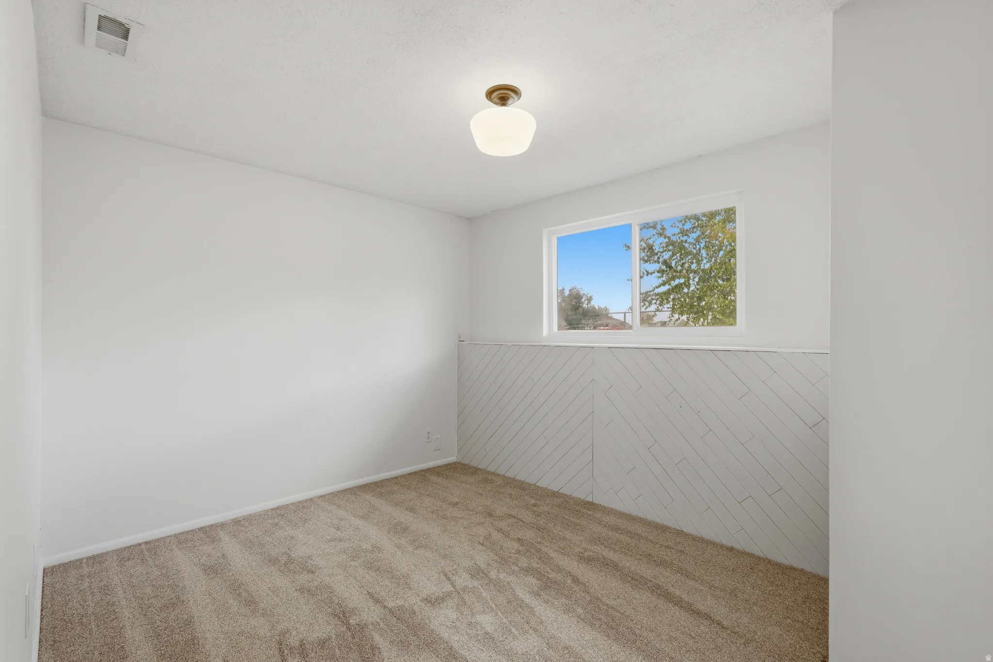 Bright room featuring a window, textured wall paneling, neutral carpet, and a ceiling-mounted light fixture