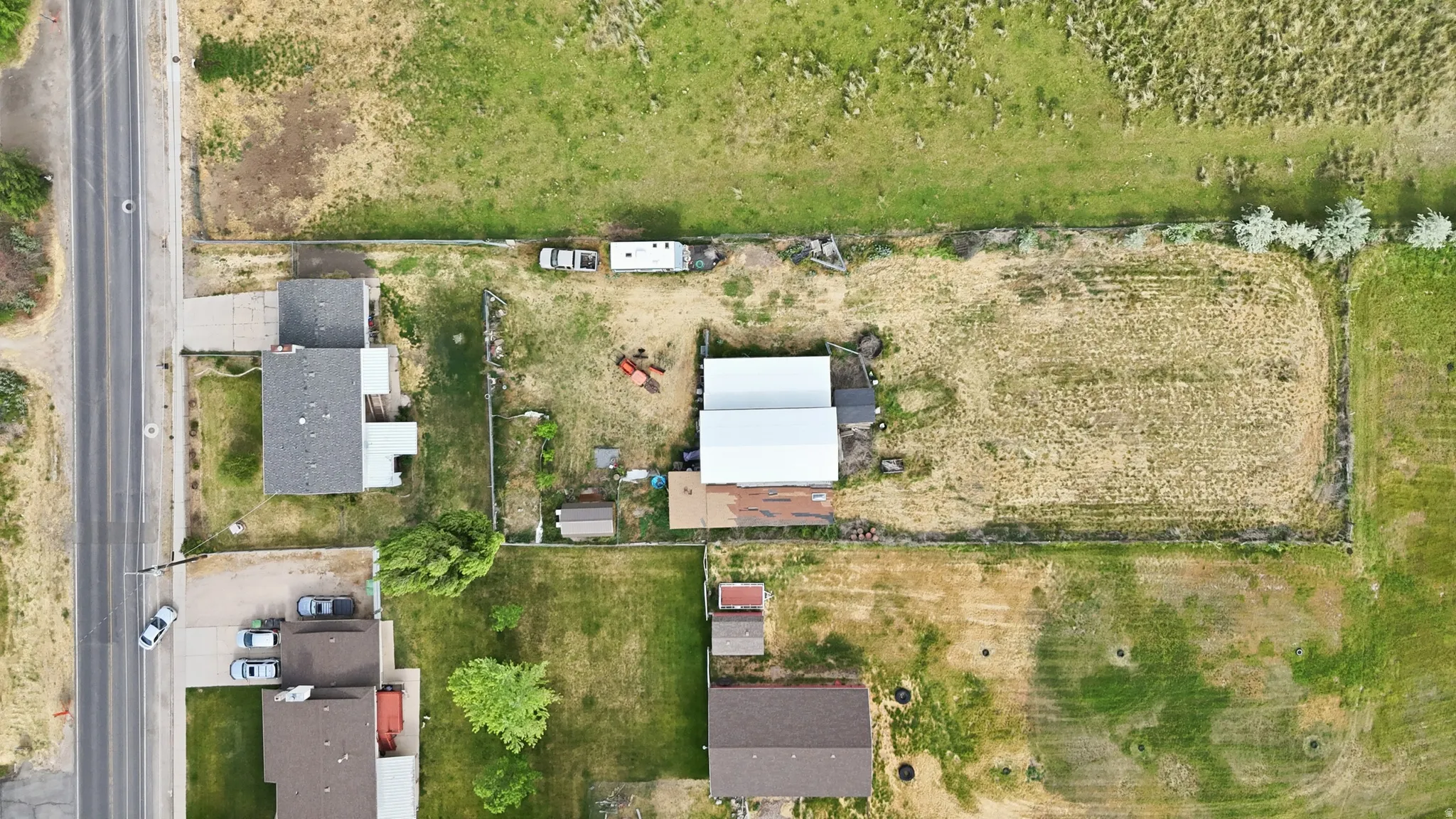 Expansive lot featuring a large open field, perimeter fencing, and a detached outbuilding