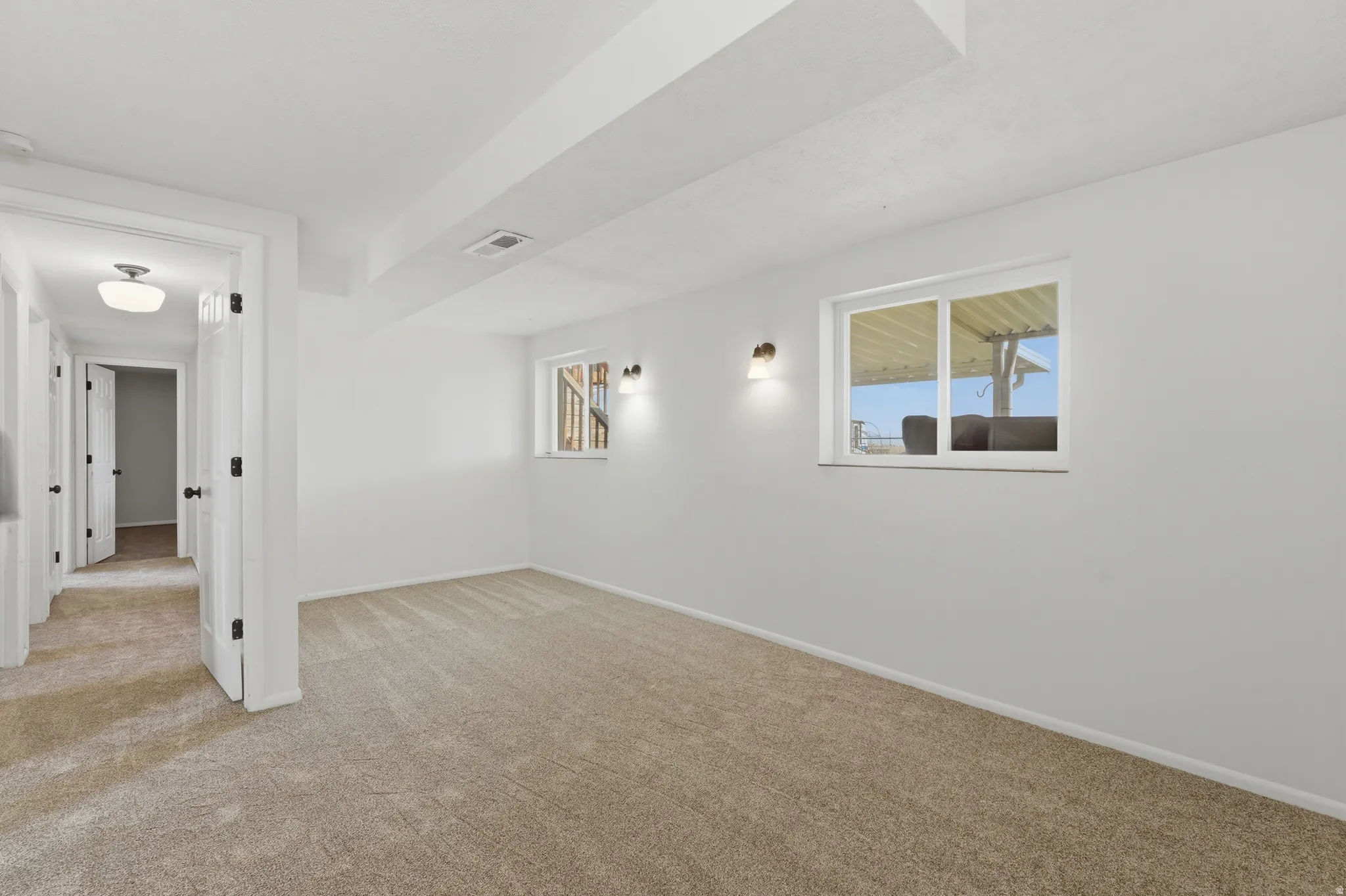 Carpeted room featuring white walls, two wall-mounted sconces, and a white-framed window