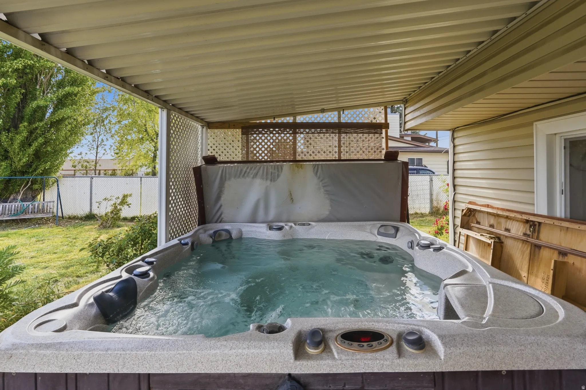 Covered outdoor spa area featuring a hot tub, slatted patio cover, and lattice privacy screen
