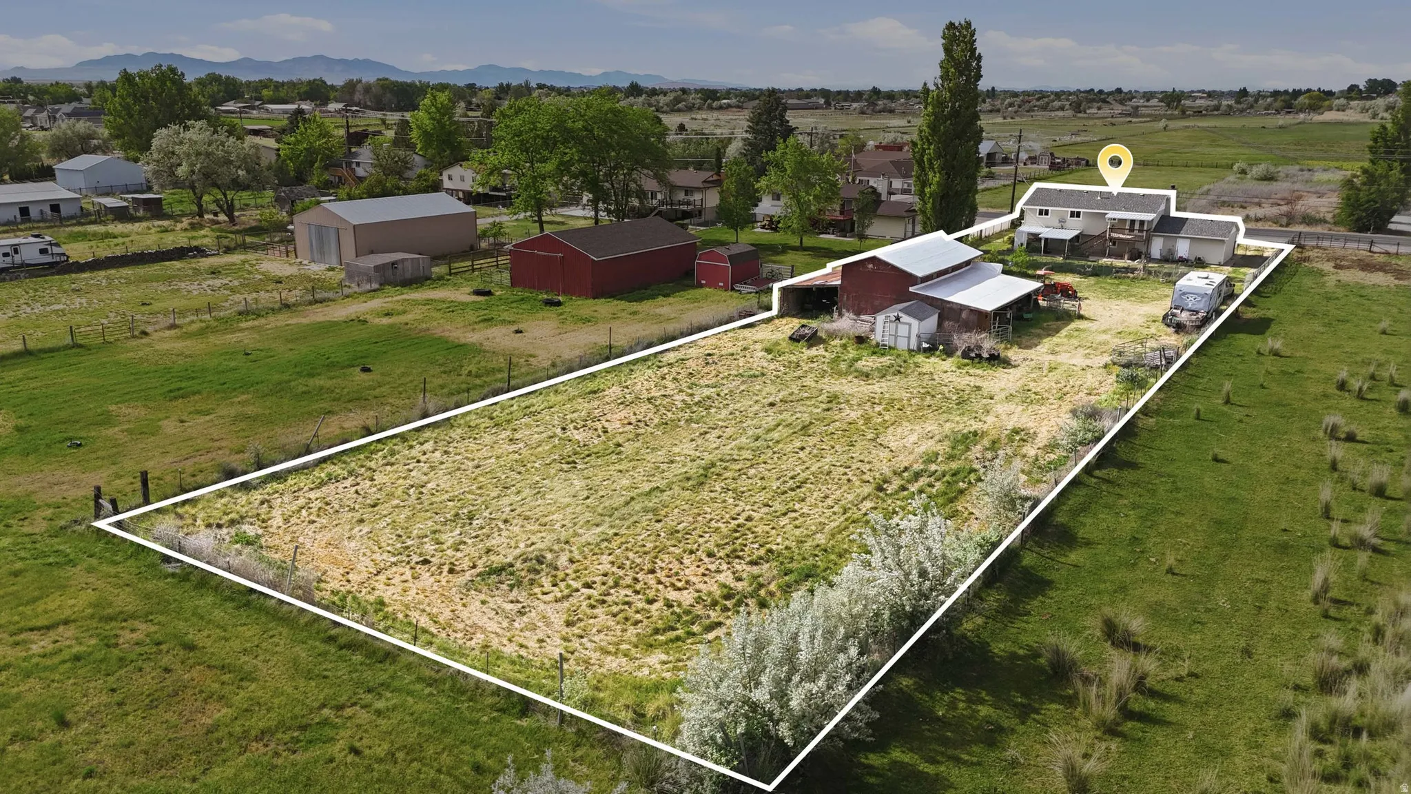 Expansive property featuring a two-story residence, multiple outbuildings, and open fields with mature trees