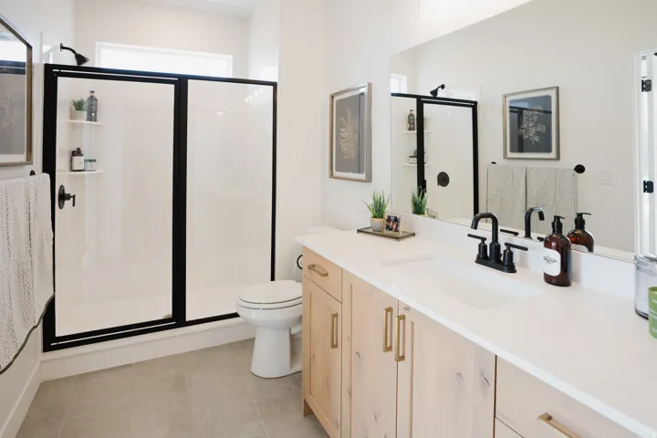 Bathroom featuring a dual-sink vanity with light wood-finish cabinetry, a white countertop, and matte black fixtures