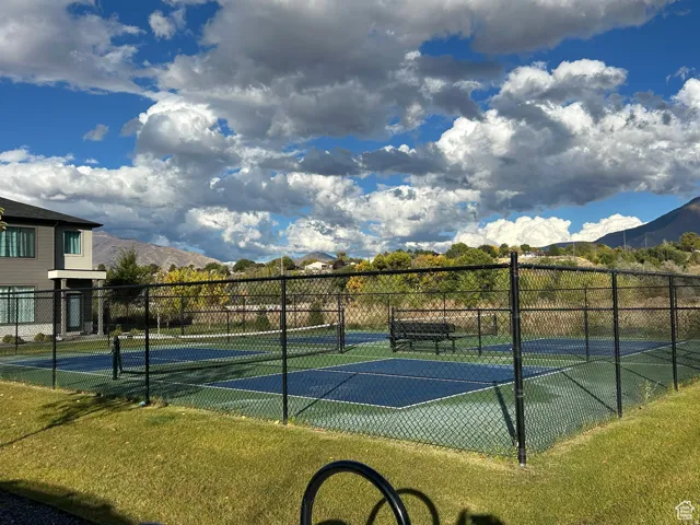 Fenced sports court with blue and green surfacing, featuring a net and a bench