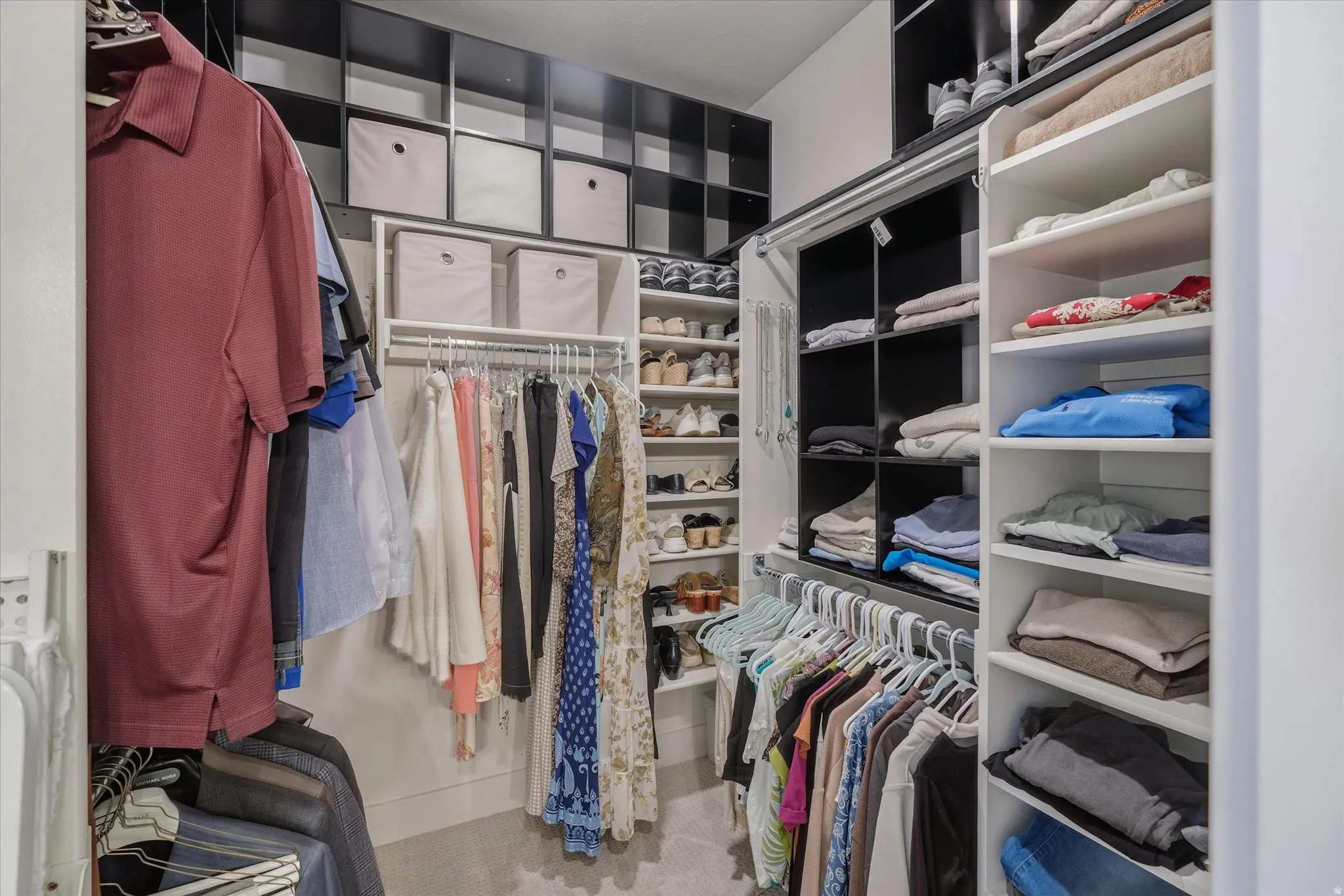 Custom closet system featuring white shelving, black cubbies, multiple hanging rods, built-in shoe racks, and ample storage compartments