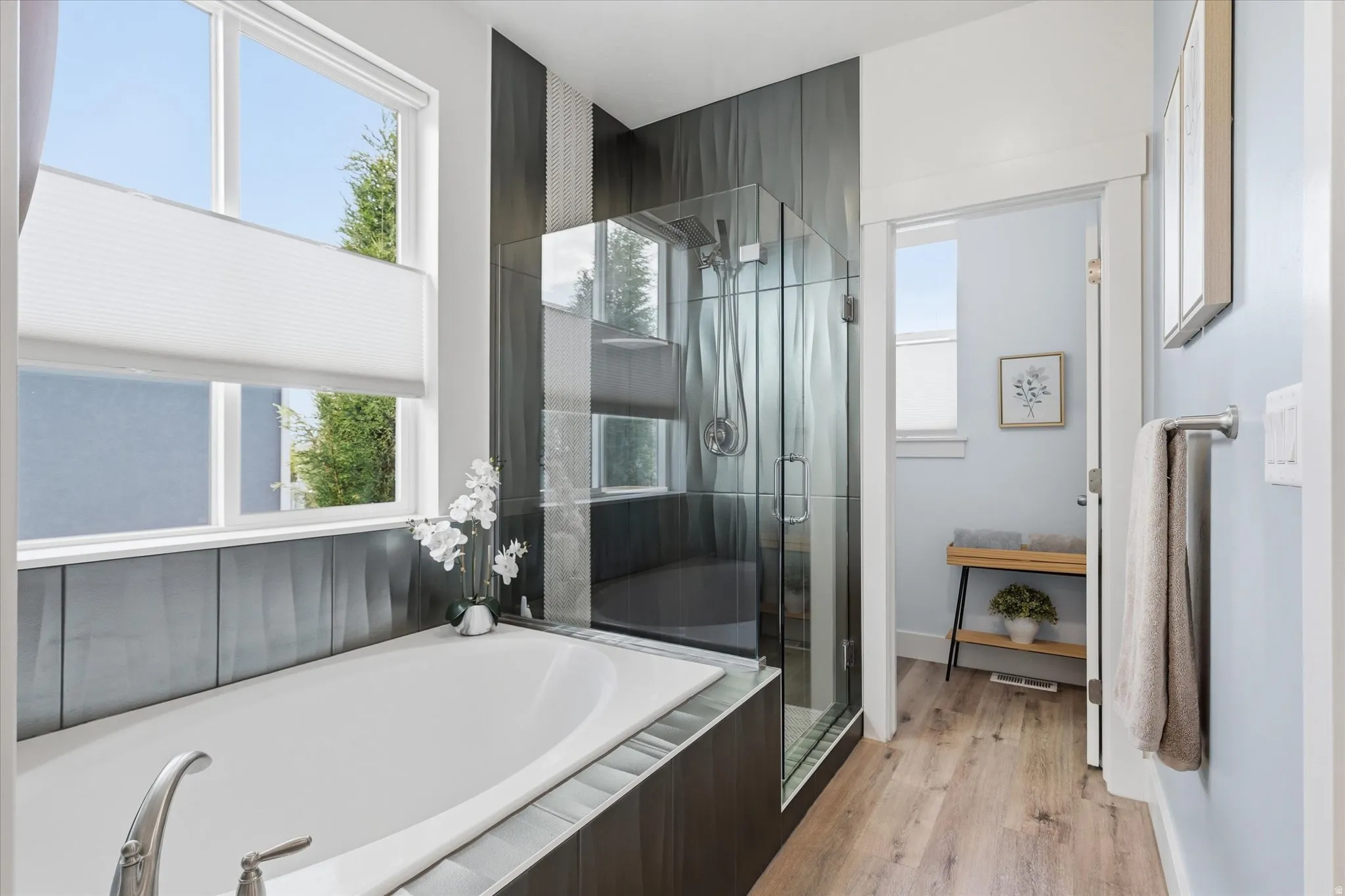 Soaking tub with brushed nickel fixtures, complemented by dark-toned tile surround and large window with privacy blinds