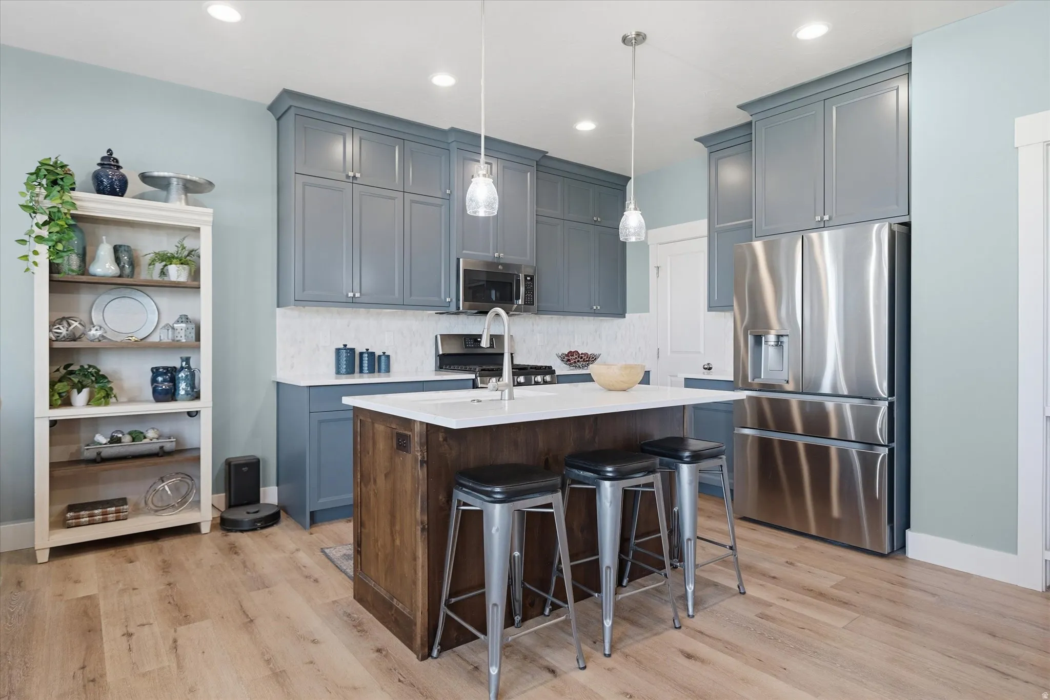 Kitchen featuring wood-finish flooring, a central island with white countertop, pendant lighting, stainless steel appliances, and grey cabinetry