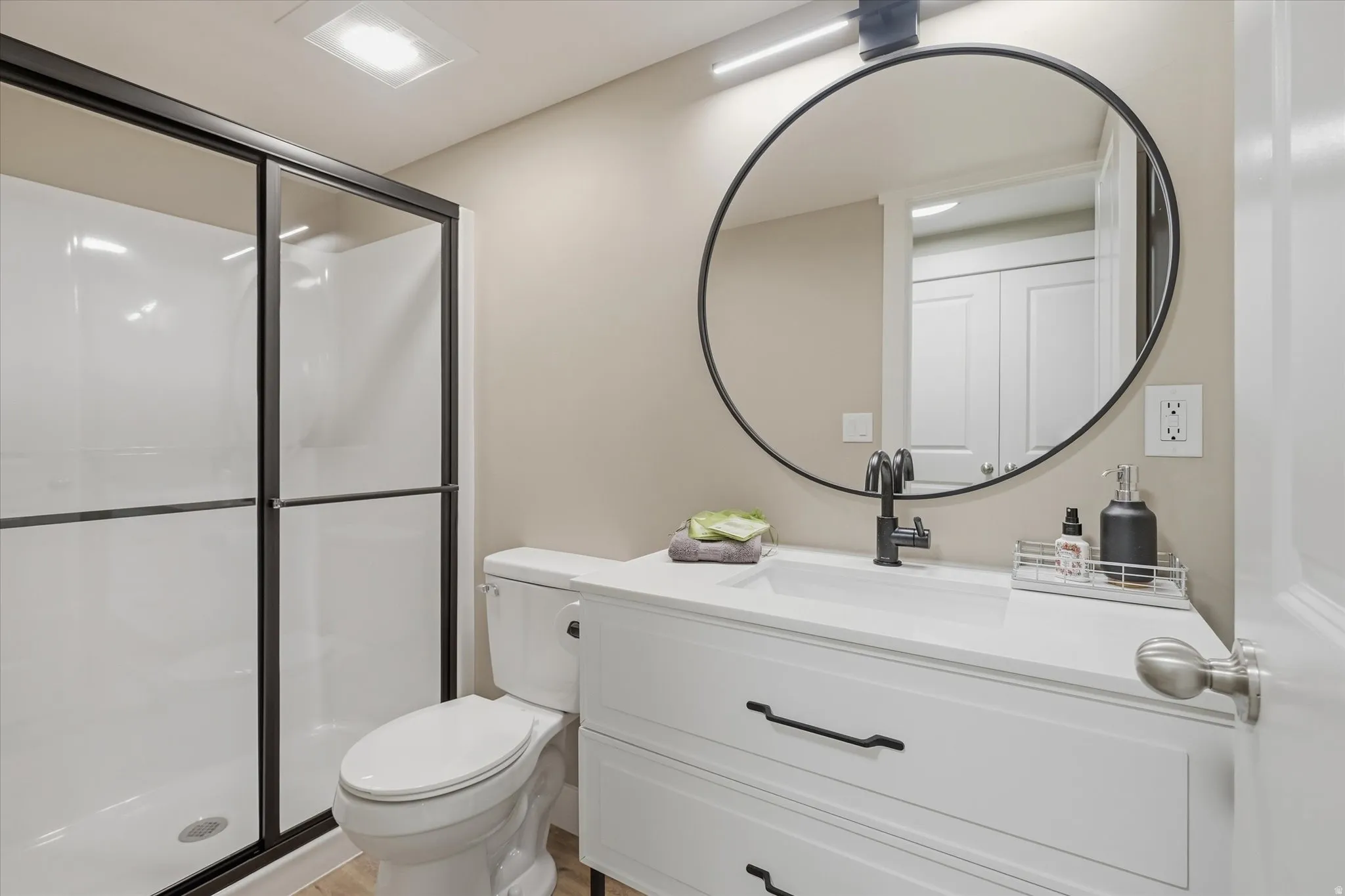 Apartment -Bathroom featuring a modern vanity with white countertop, round black-framed mirror, and matte black faucet