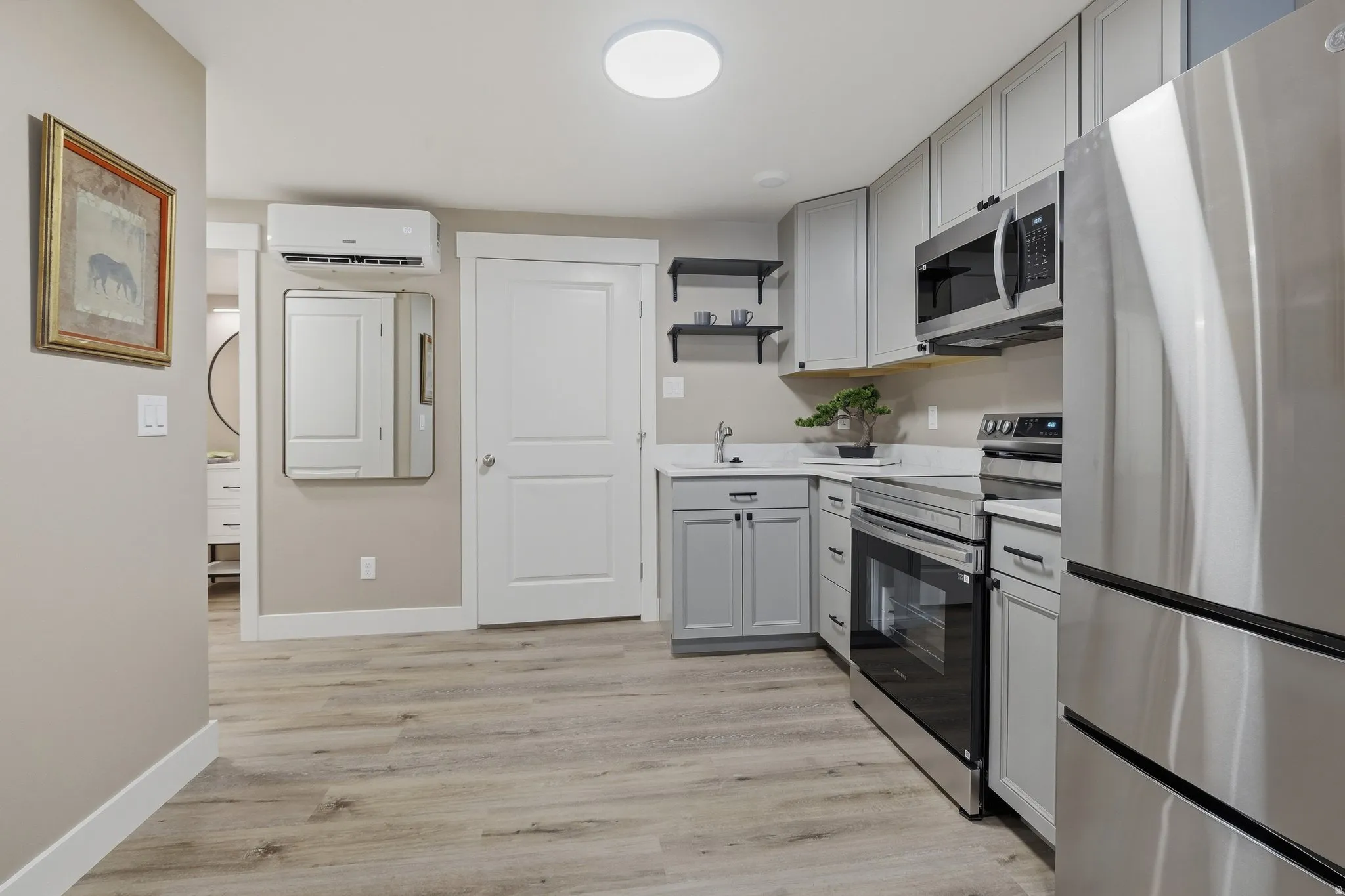 Modern kitchen featuring stainless steel appliances, light gray cabinetry, quartz-finish countertops, and wood-finish flooring